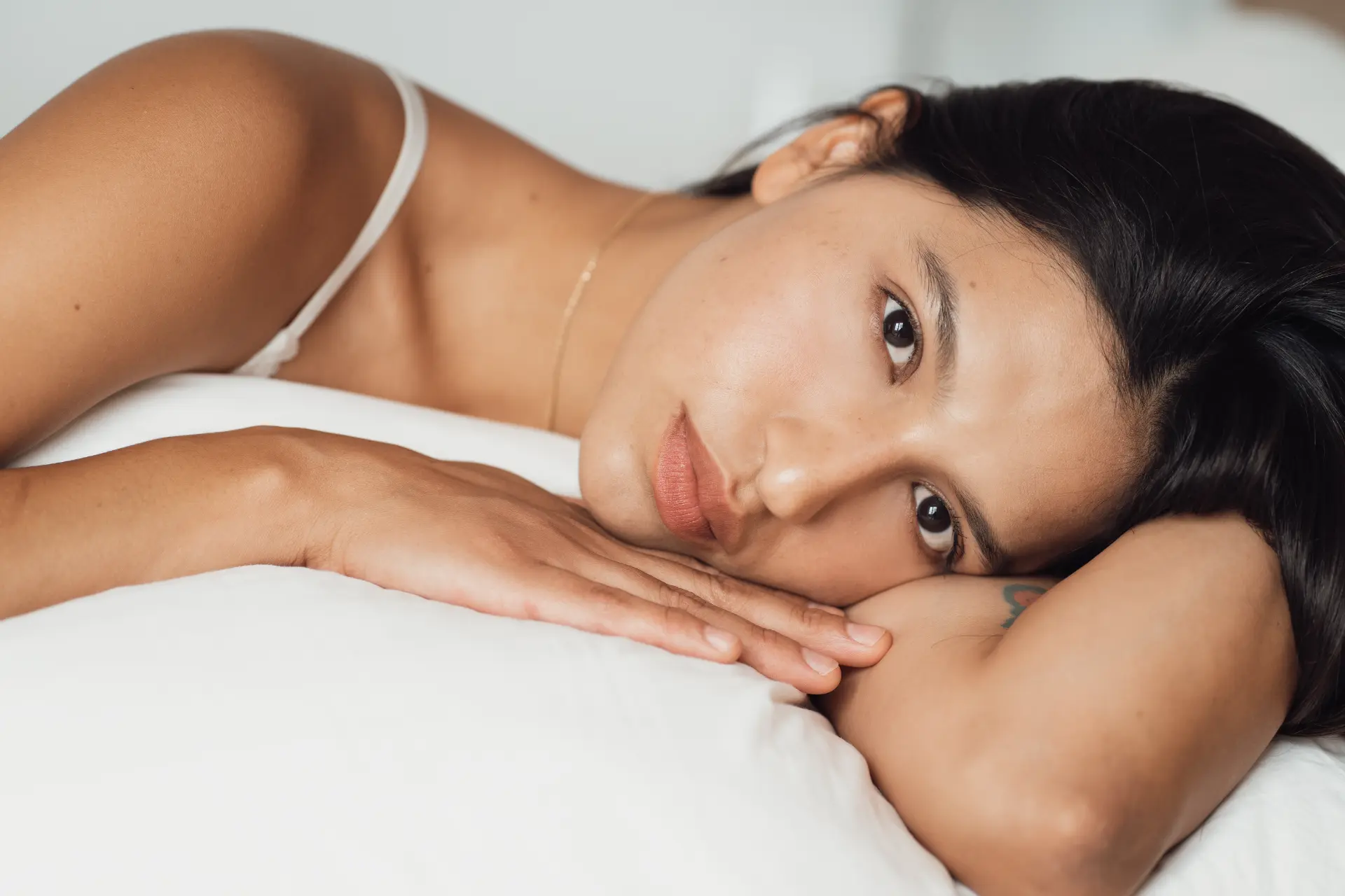 Woman resting her head on her hands on white bedding