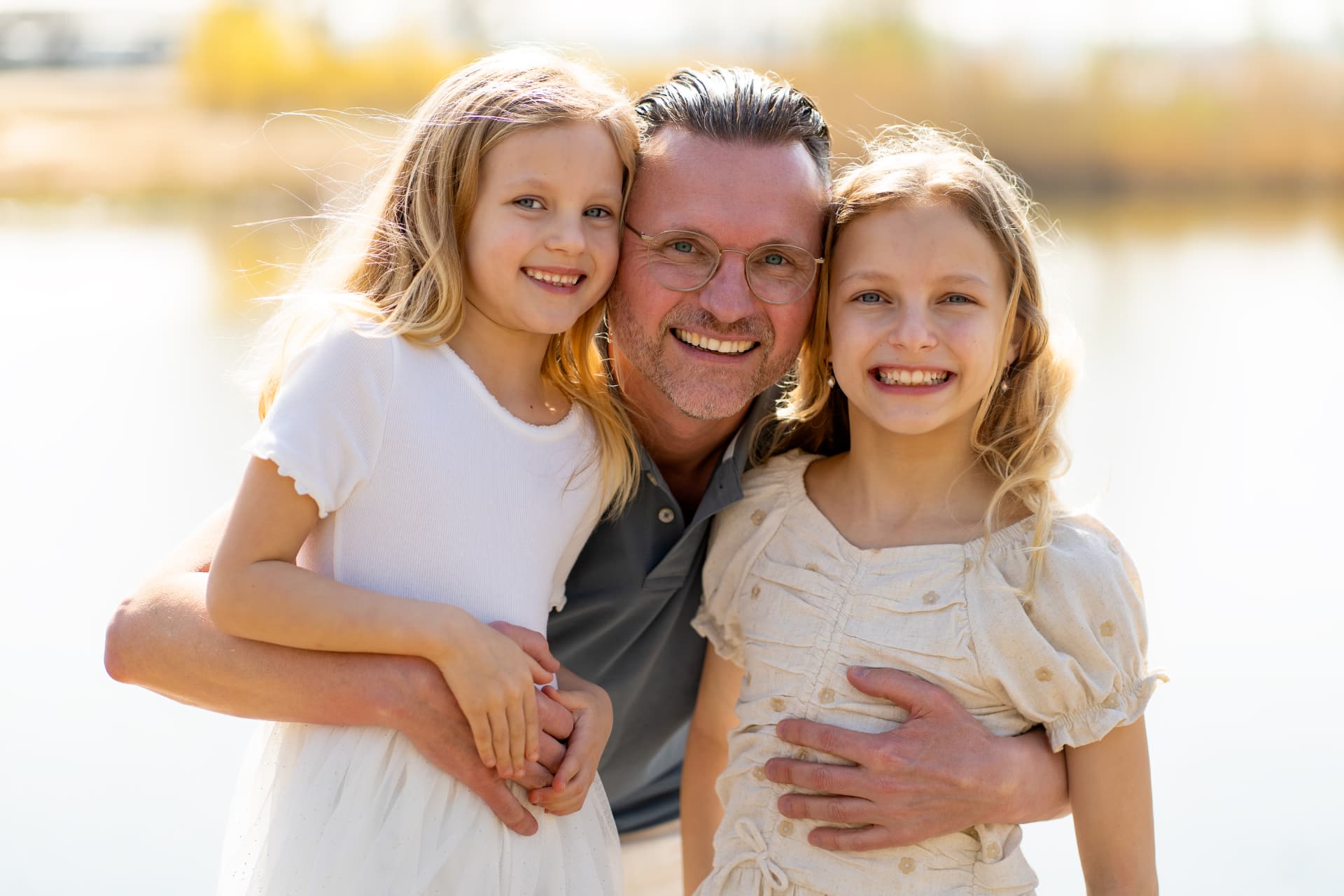 Father holding his two daughters close, all smiling into the camera