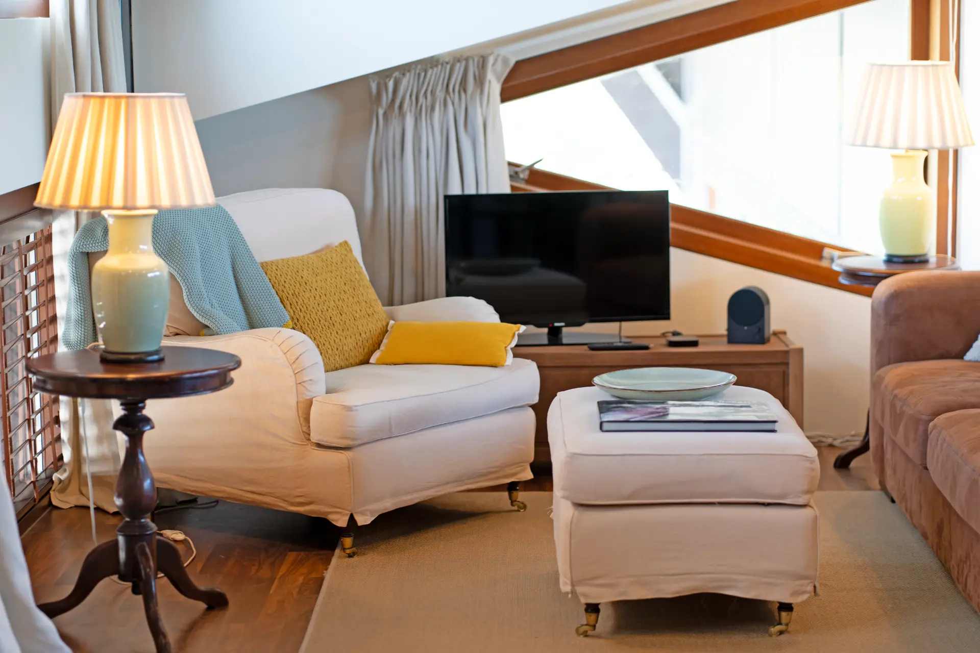 A cream armchair with yellow cushions beside the television
