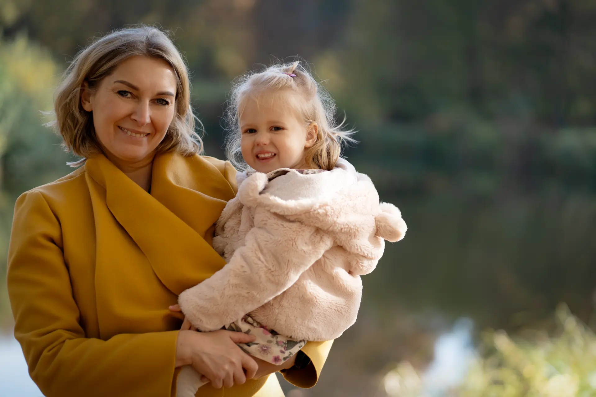 Mother holding her daughter beside the autumn lake