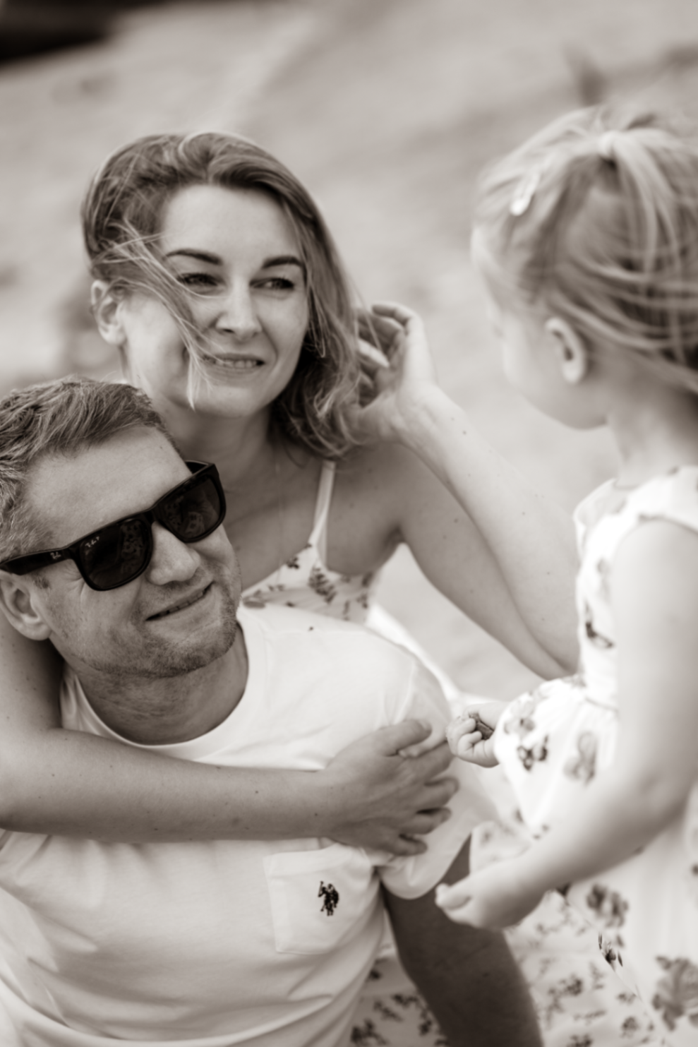 Parents laughing together on the sand while their daughter reaches in