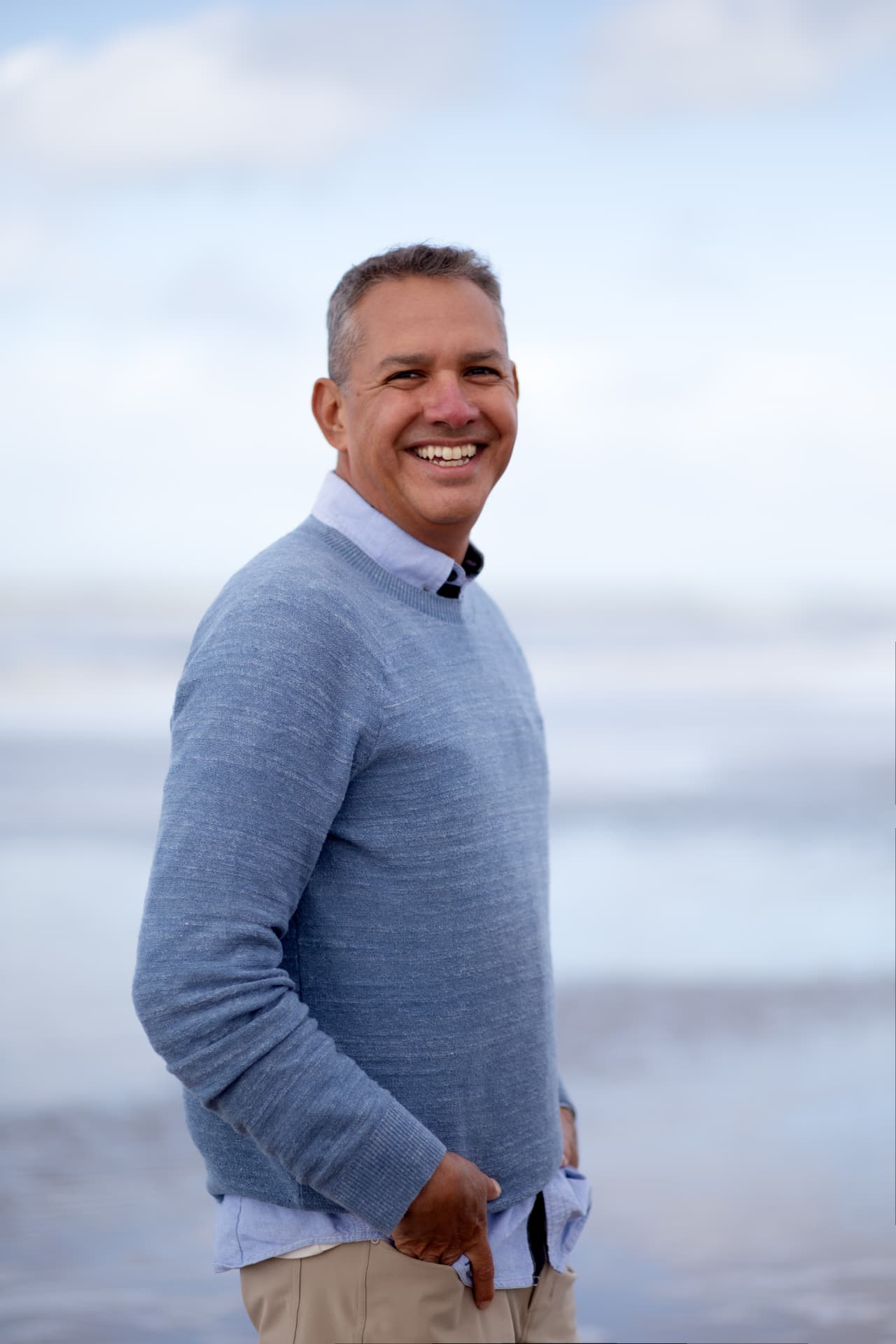 Rey smiling beside the sea in a soft blue sweater