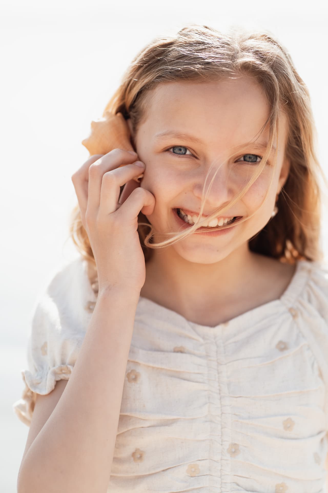 Girl holding a shell to her ear, hair blowing in the wind
