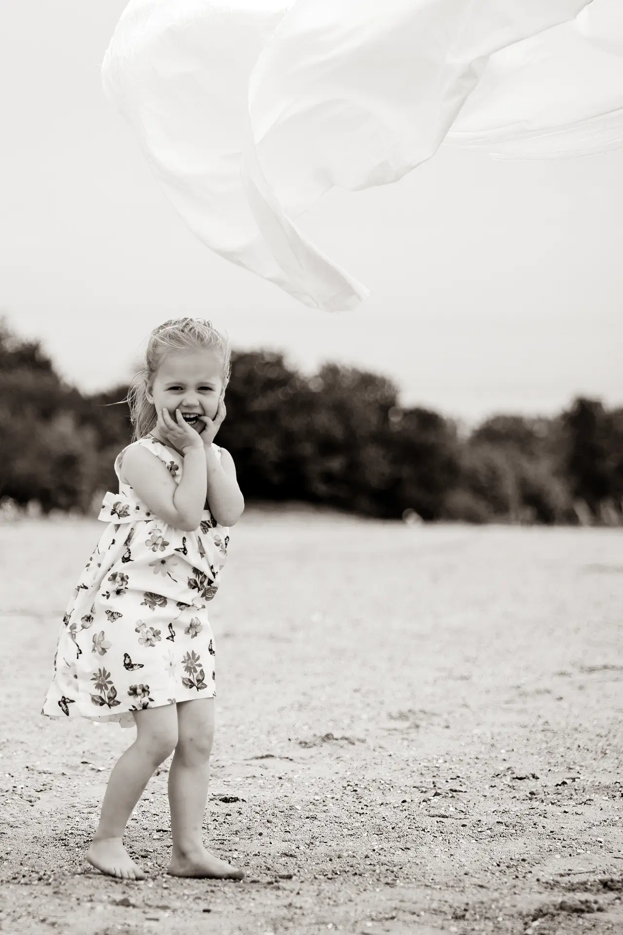 Girl laughing with her hands to her cheeks under a floating white sheet