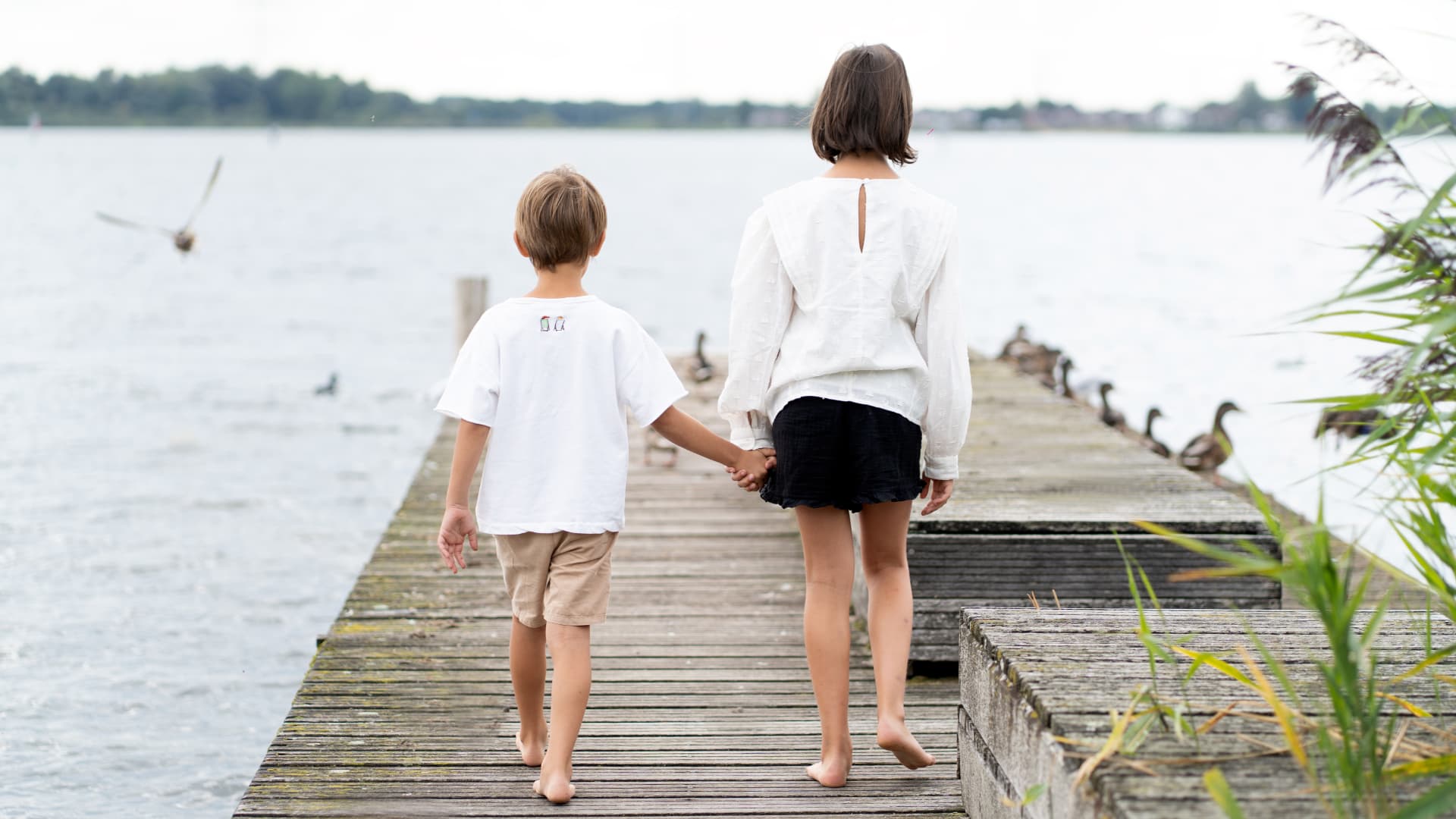 A brother and sister walking hand in hand along a wooden jetty