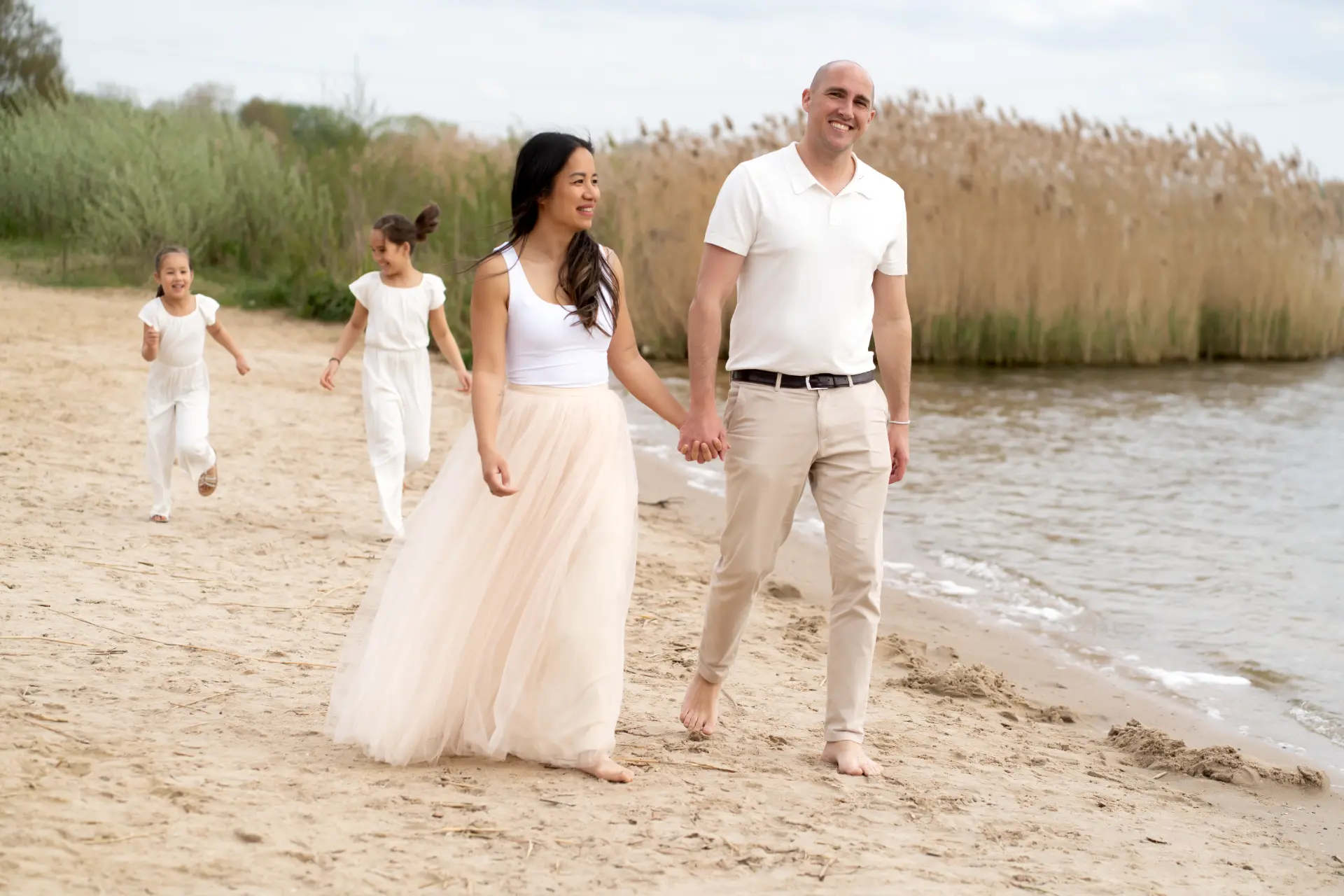 Parents walking hand in hand along the shore with their daughters behind