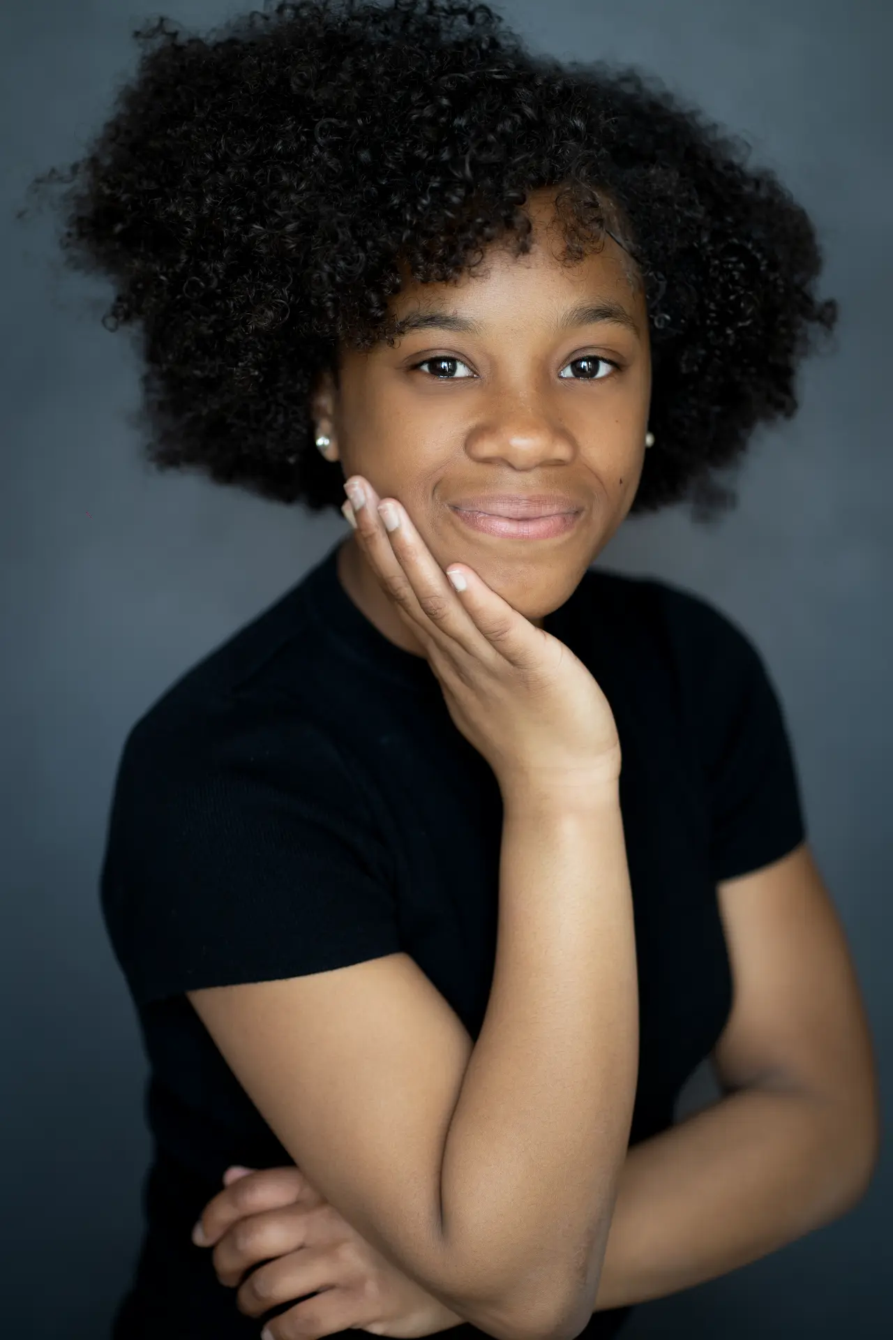 Teenager with curly hair resting her chin on her hand against a grey backdrop