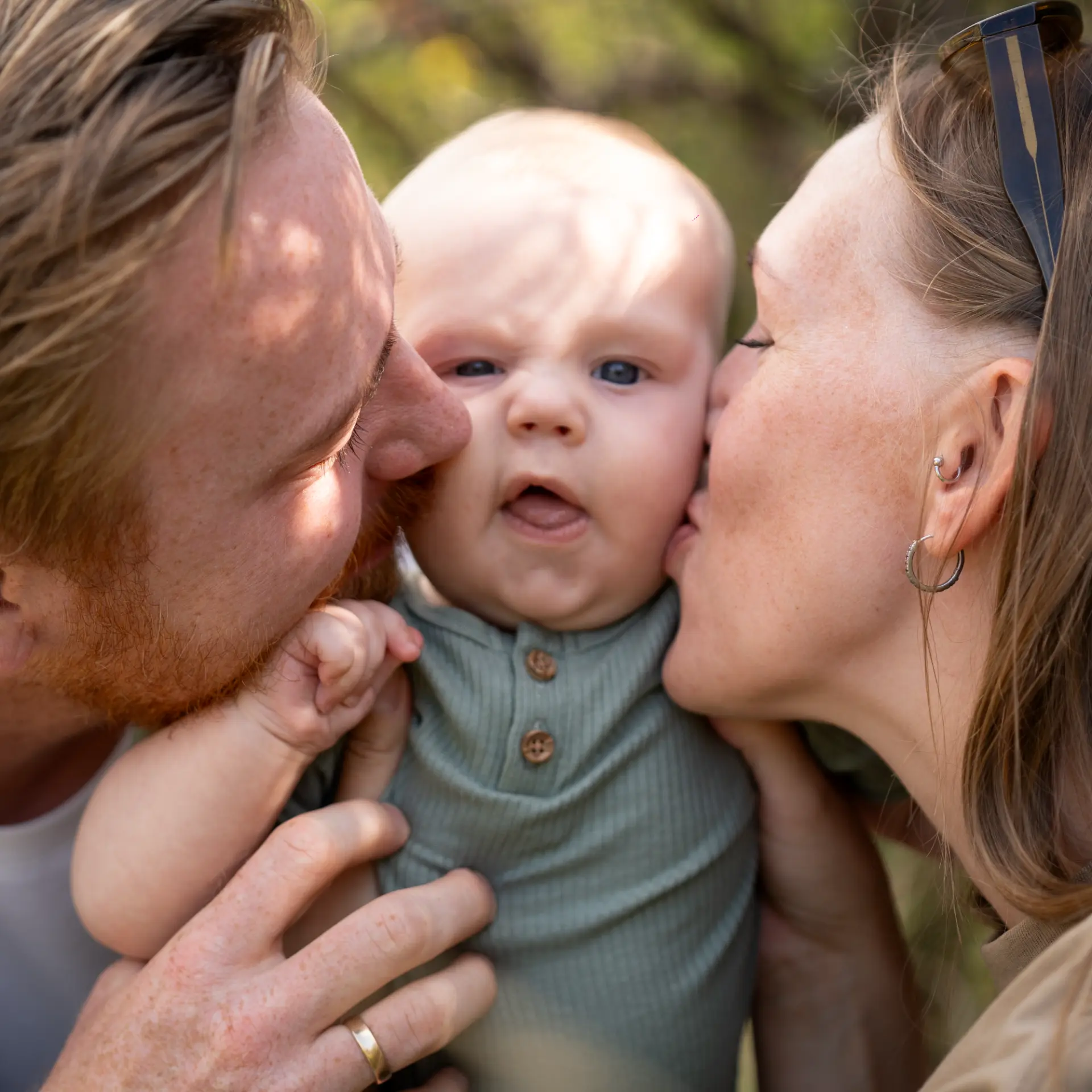 Both parents kissing their baby on the cheeks