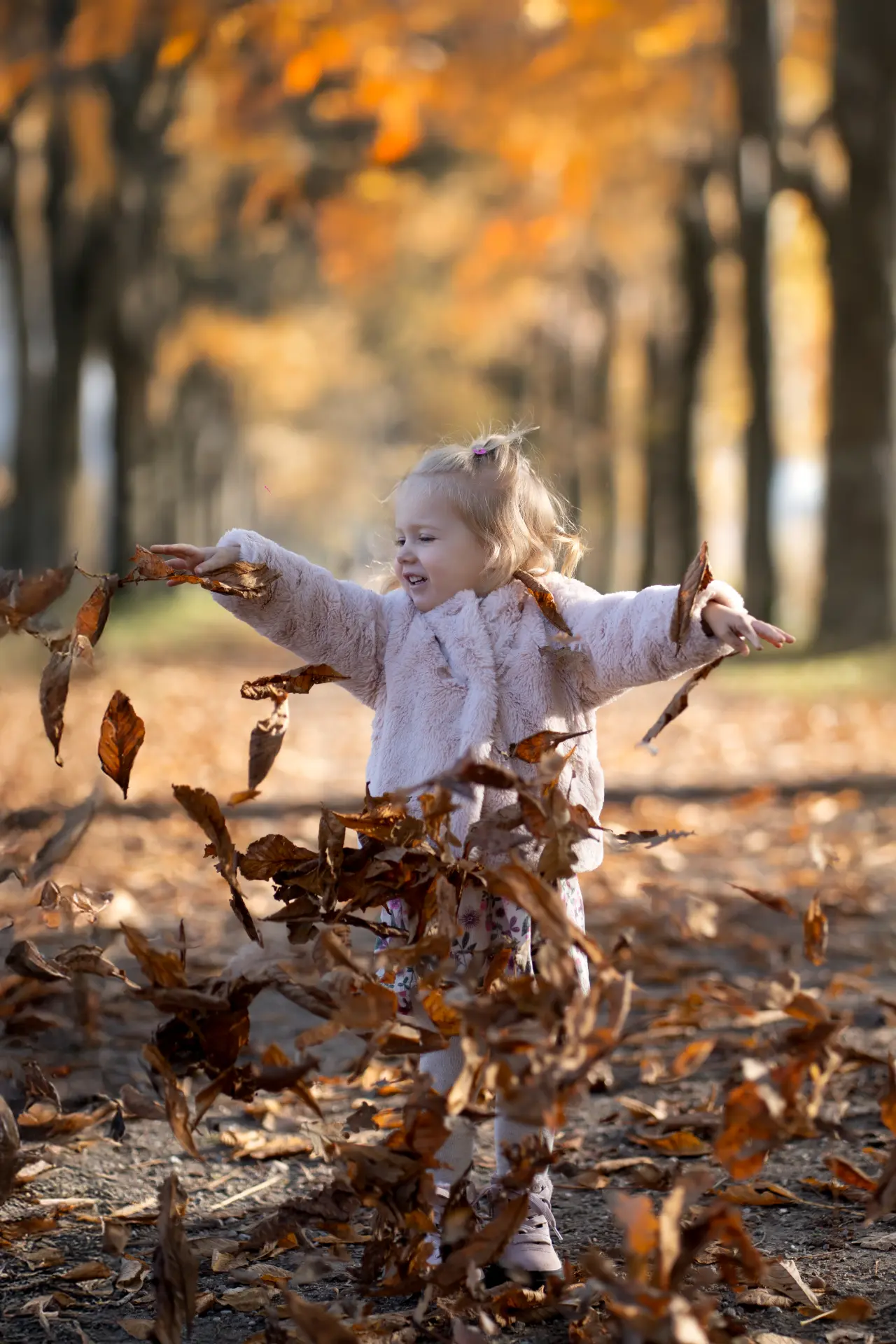 Young girl playing with fallen leaves in golden autumn light