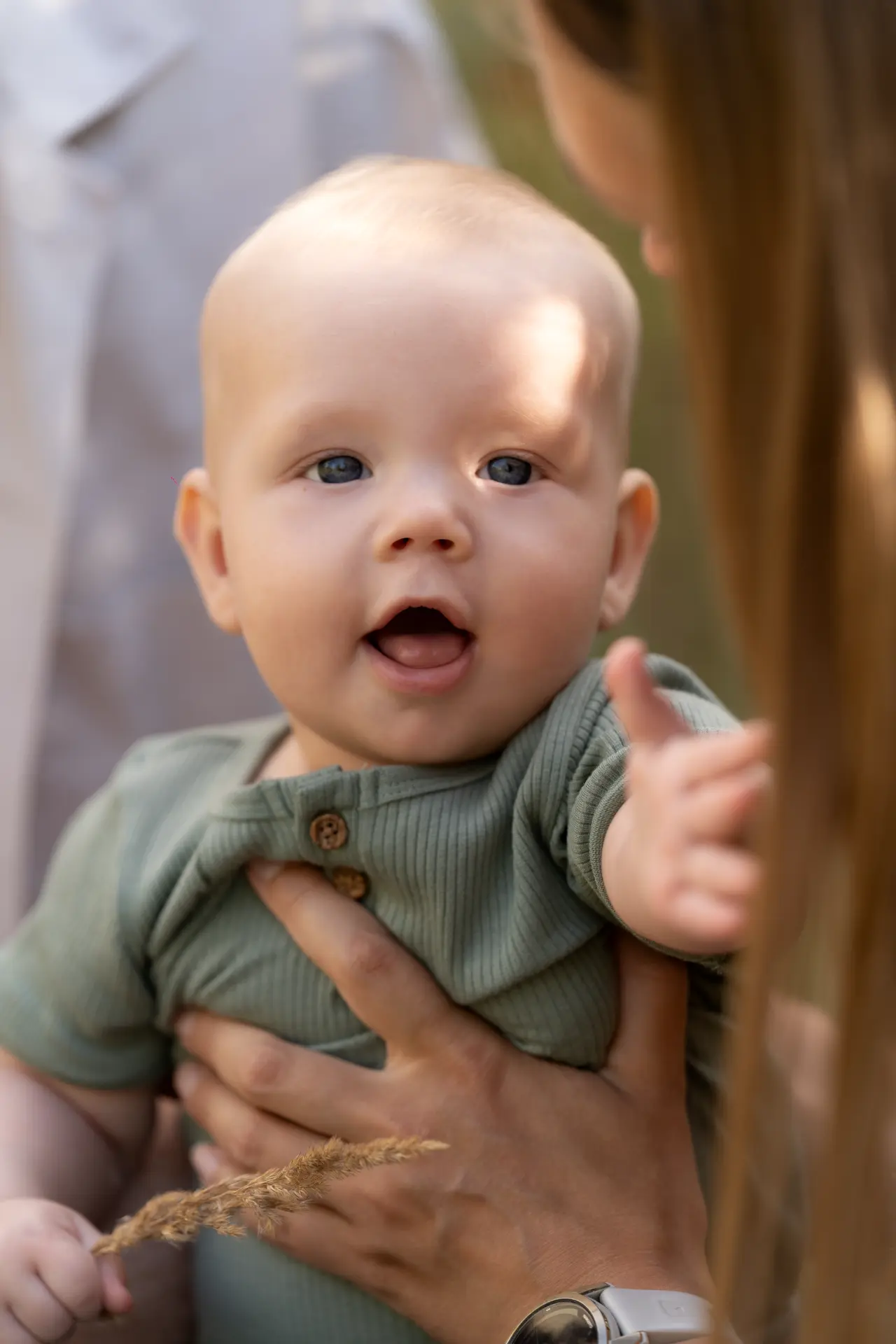 Baby in a green romper held up between his parents