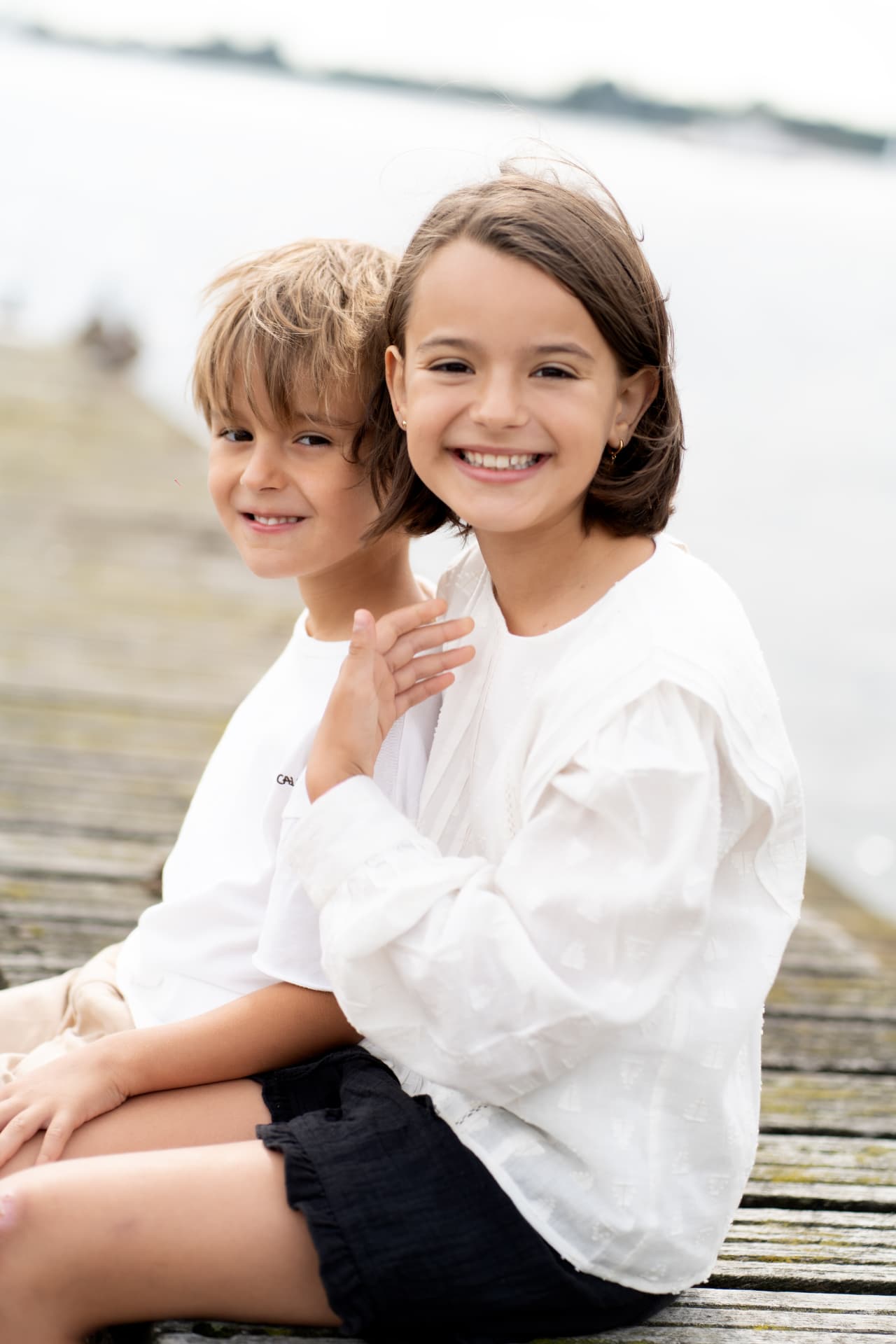 Brother and sister sitting close together on a jetty by the water