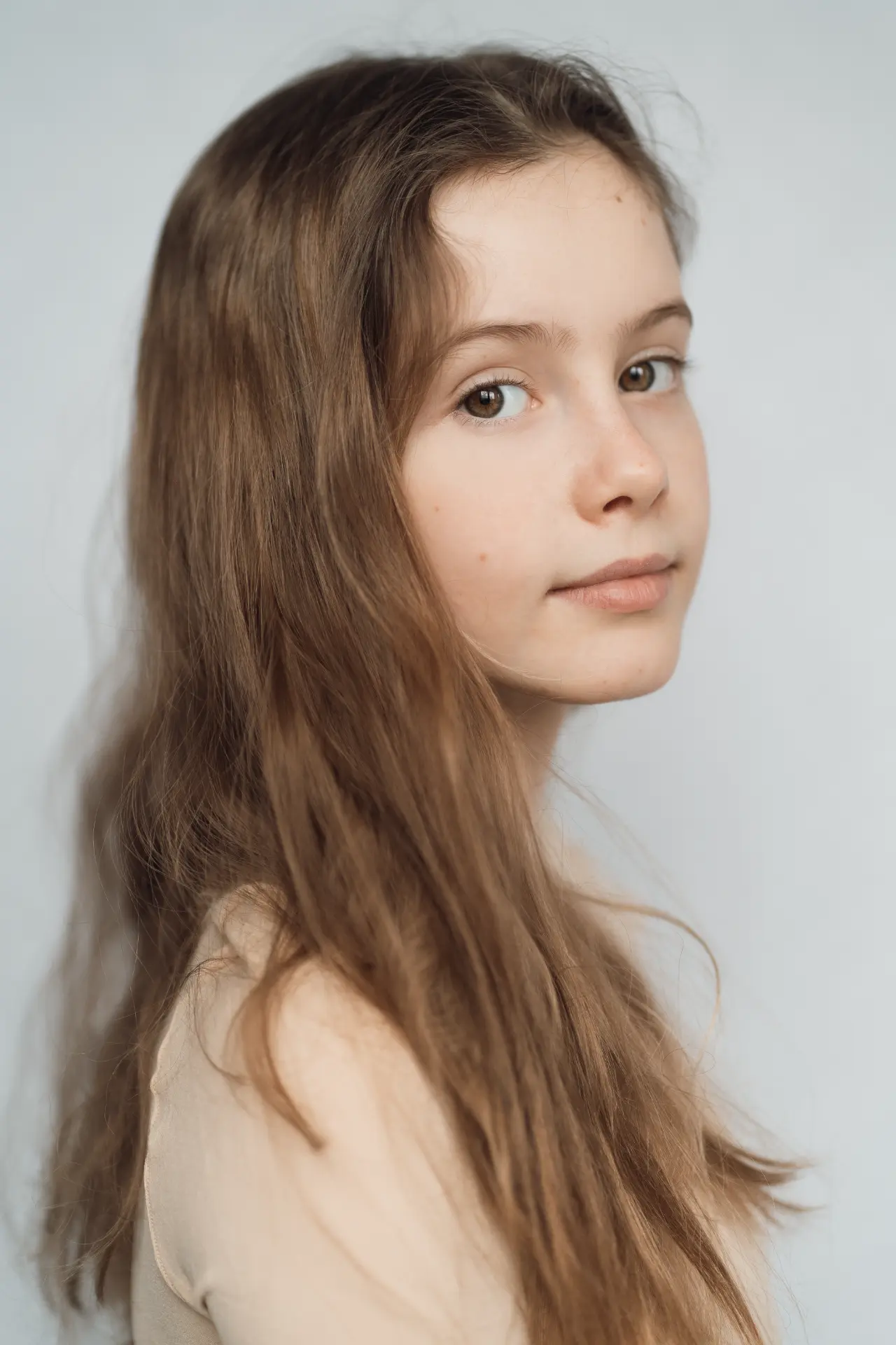 Close portrait of a girl with long brown hair against a soft pale backdrop