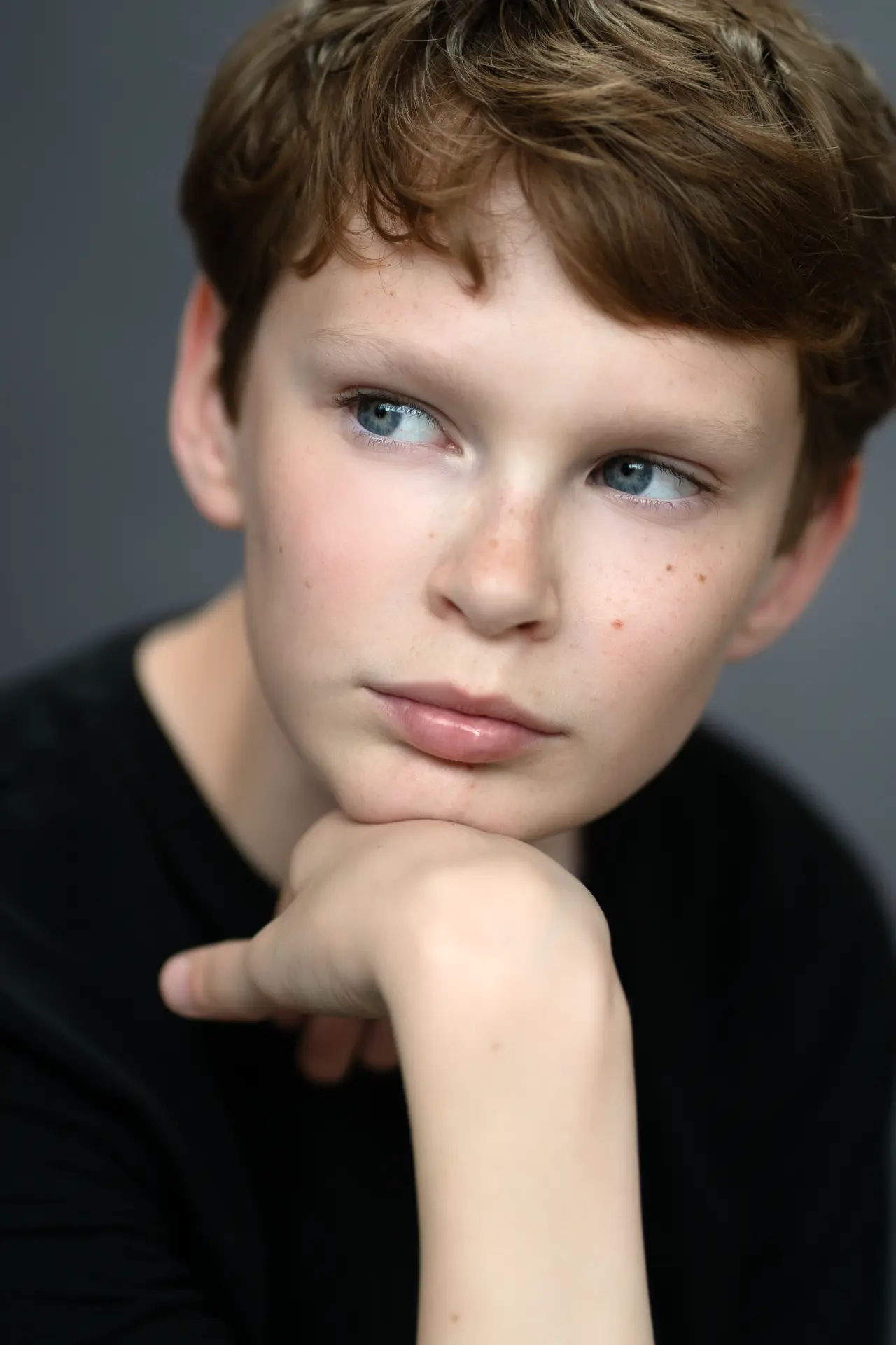 Boy in black resting his chin on his hand against a grey backdrop