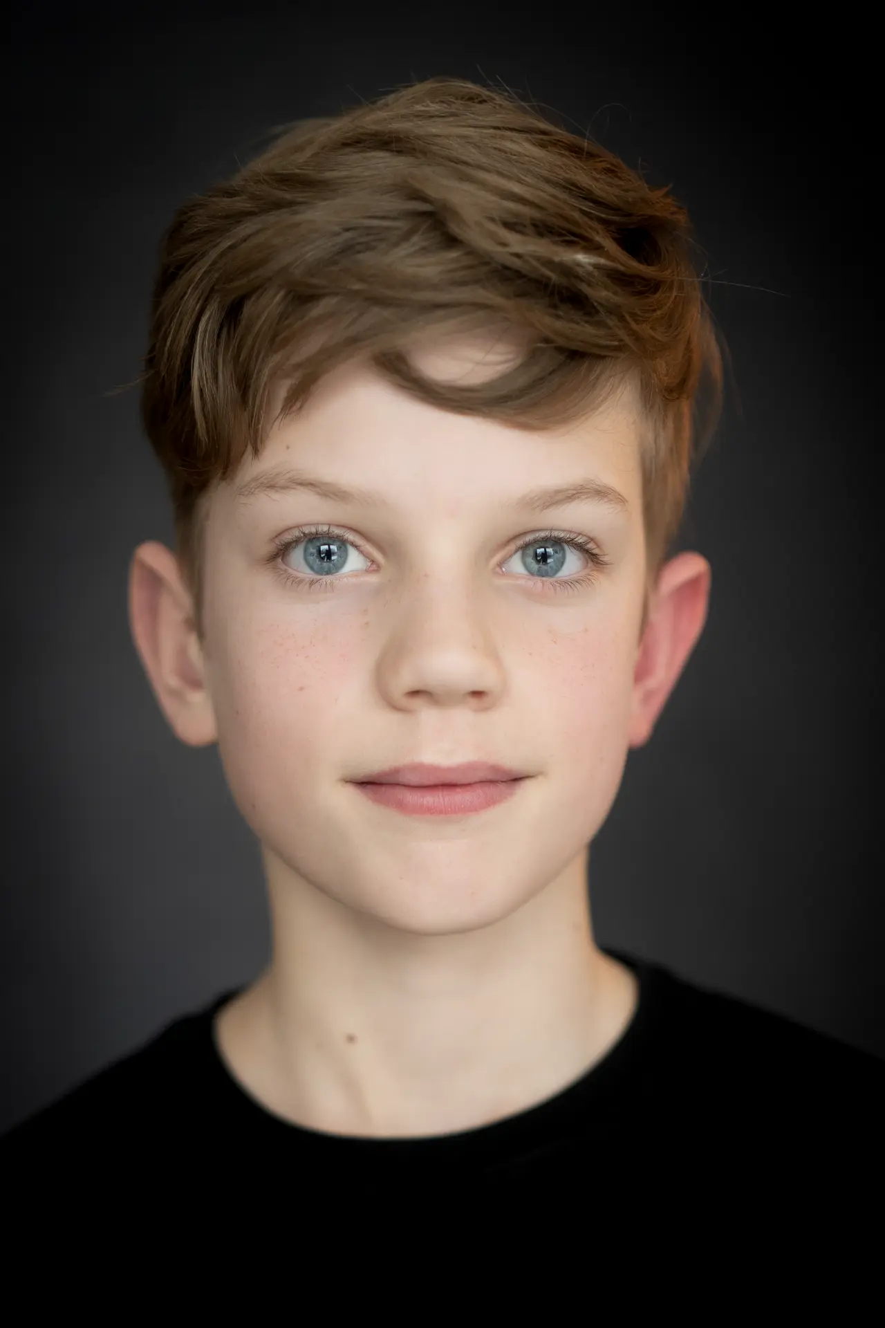 Boy in a black shirt looking into the camera against a dark backdrop