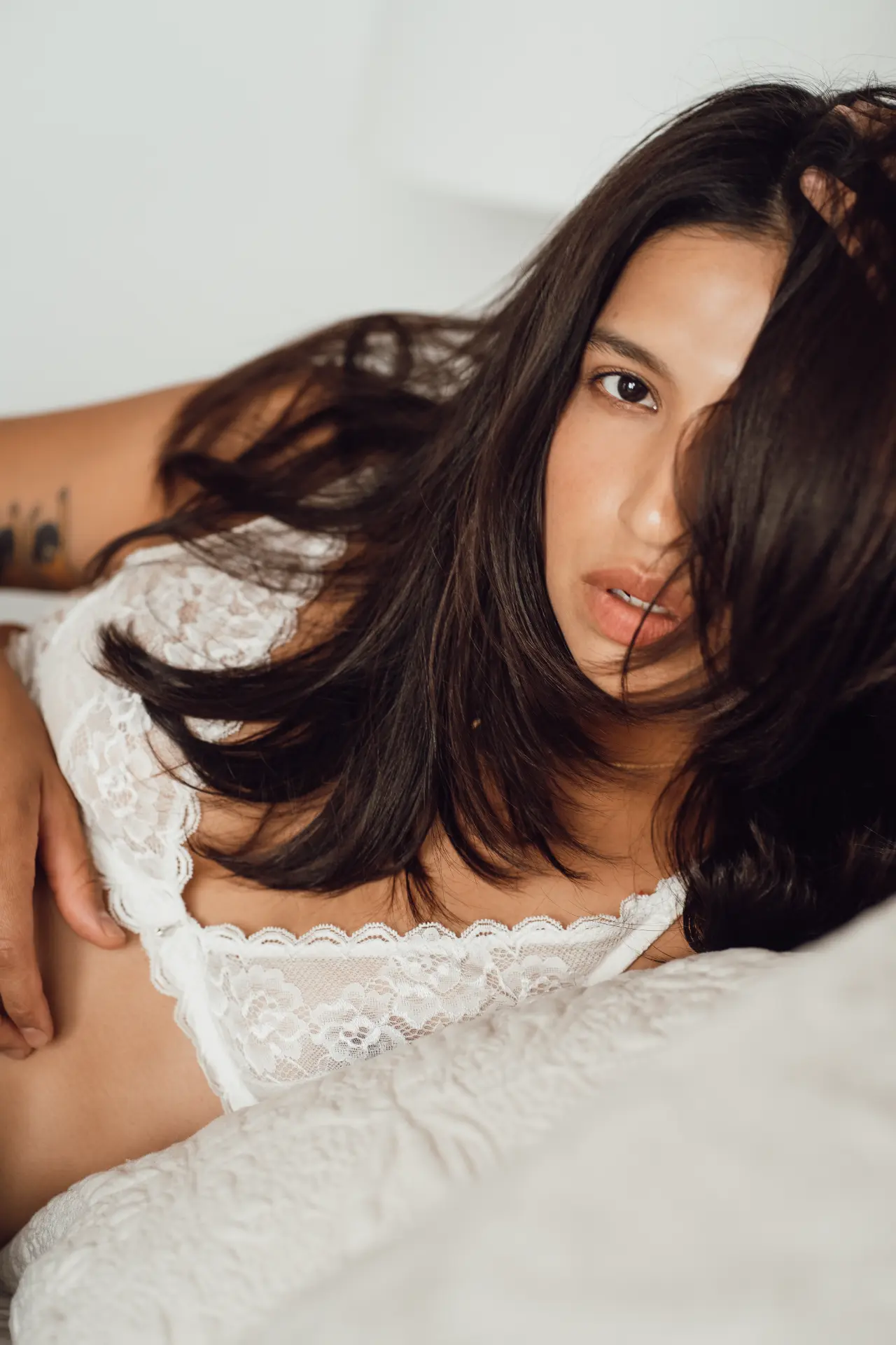 Woman in white lace resting on bright white bedding