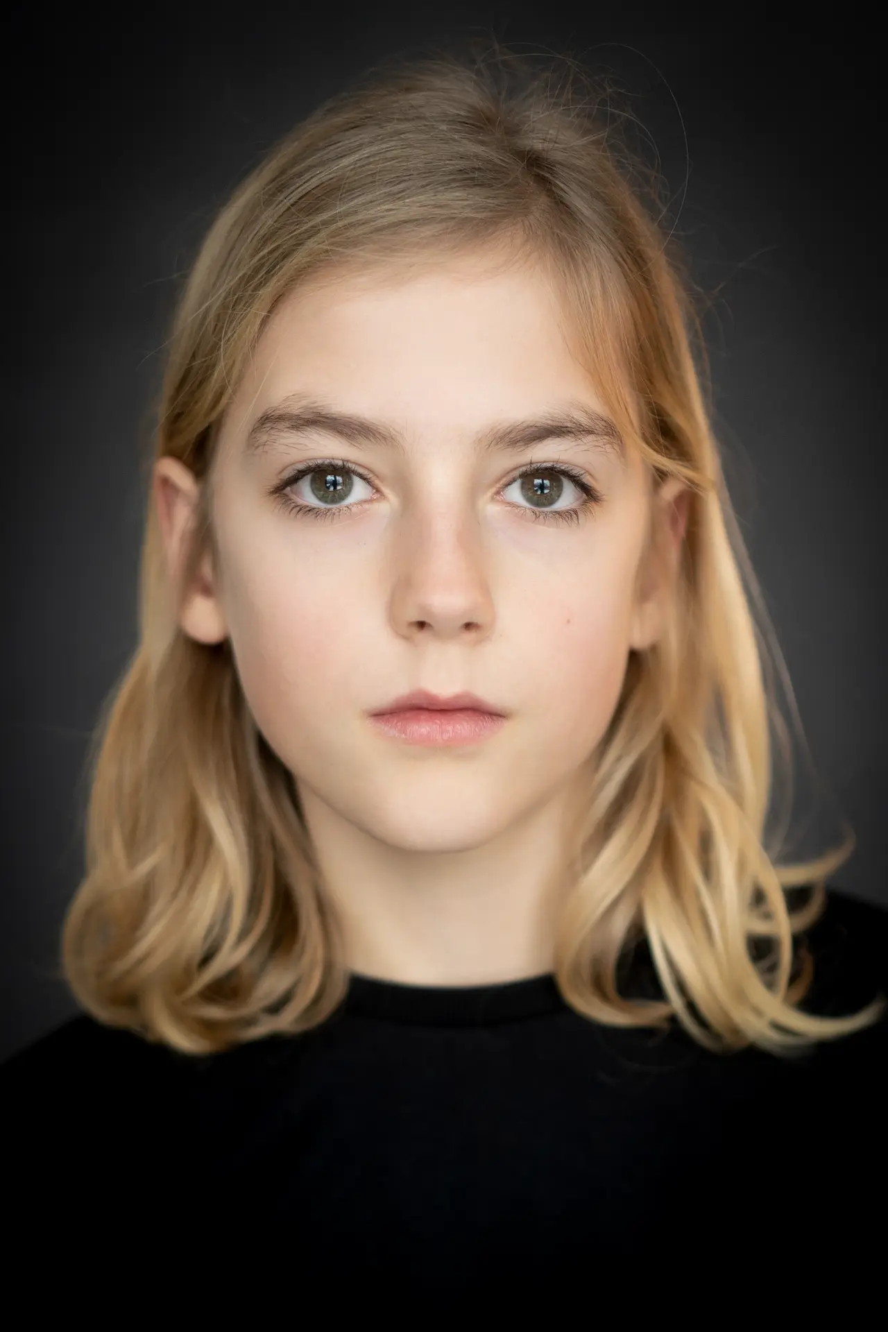 Blonde girl in black with a calm expression against a dark backdrop