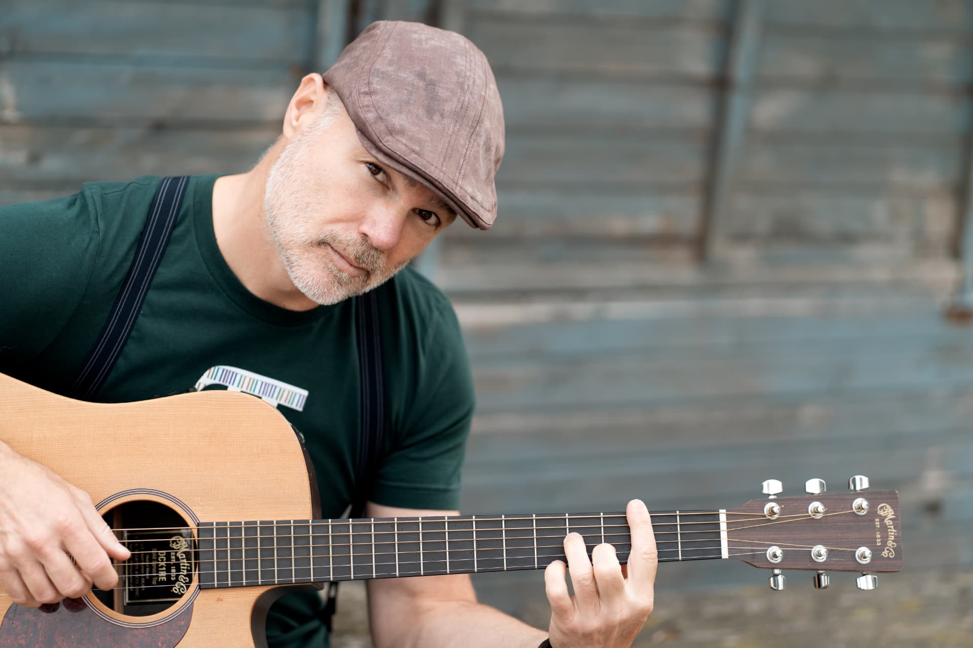 Peter playing guitar against a weathered wooden wall