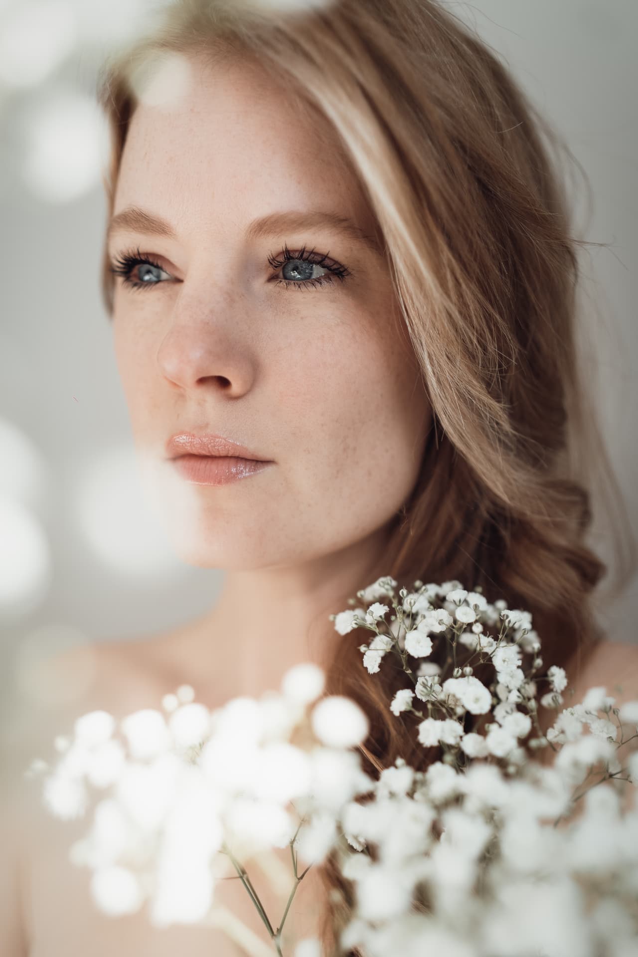 Close portrait of a woman with flowers against a softly lit ivory backdrop
