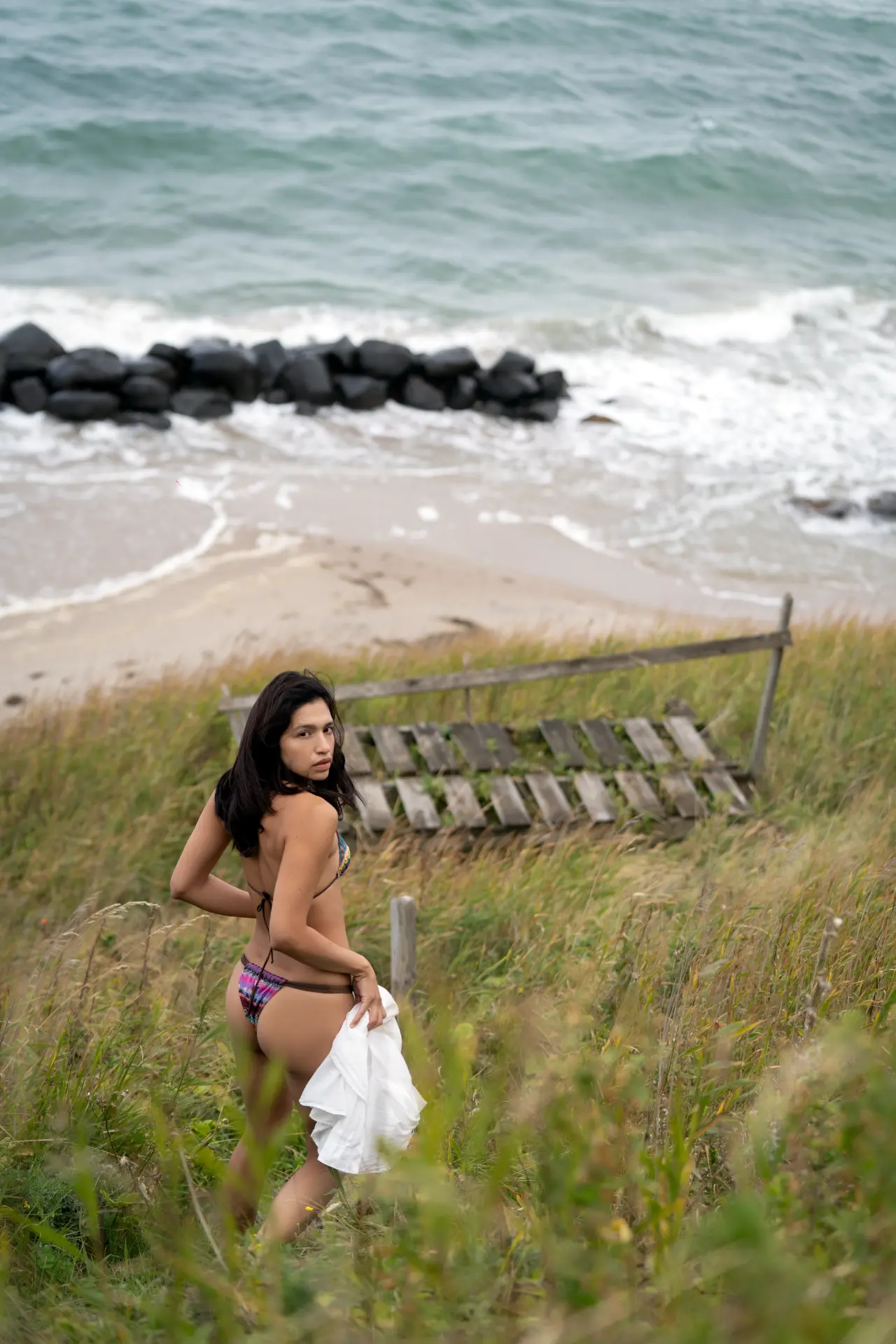 Ana walking up through tall grass from the beach, looking back