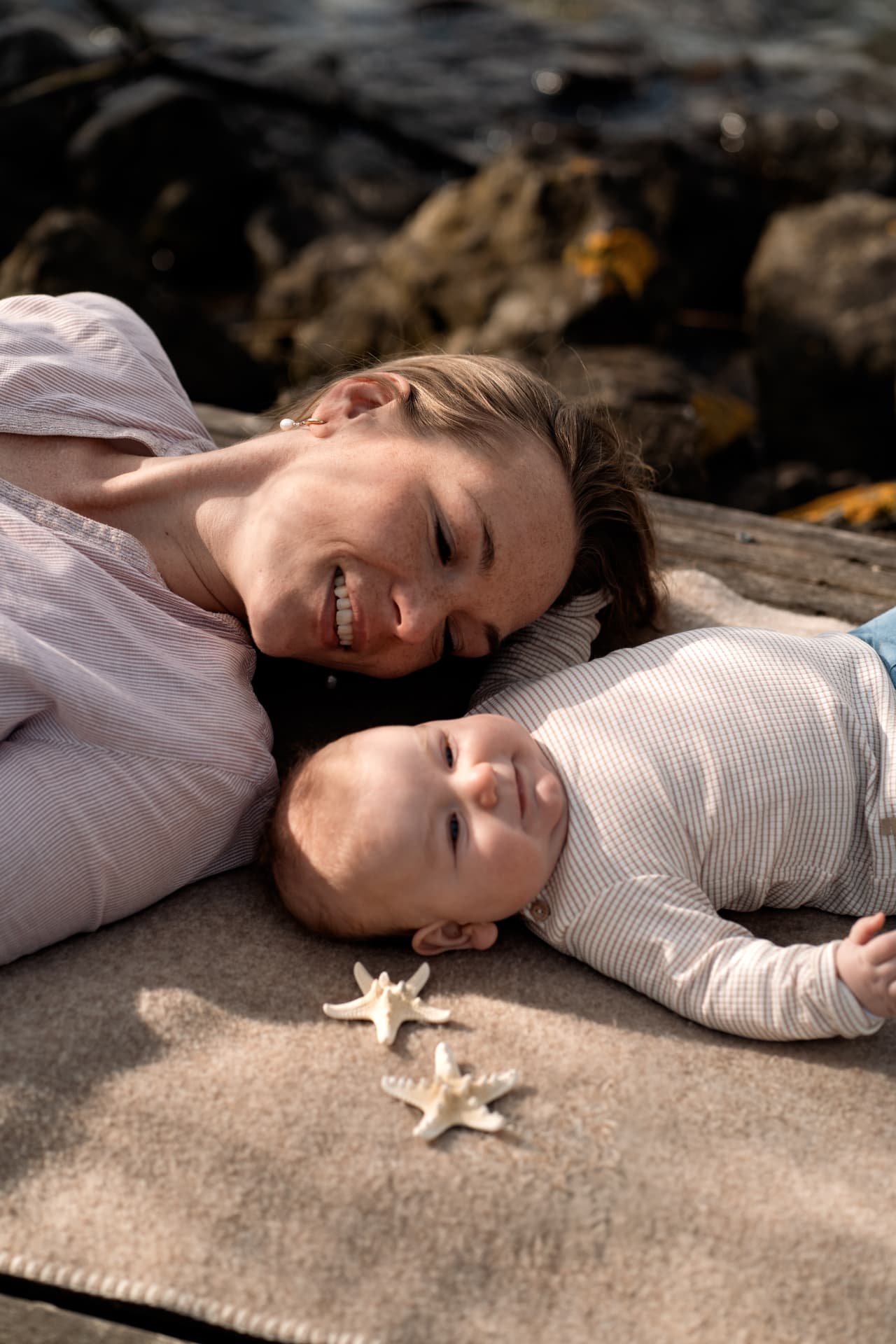 Mother and baby lying together on a blanket with starfish on the shore