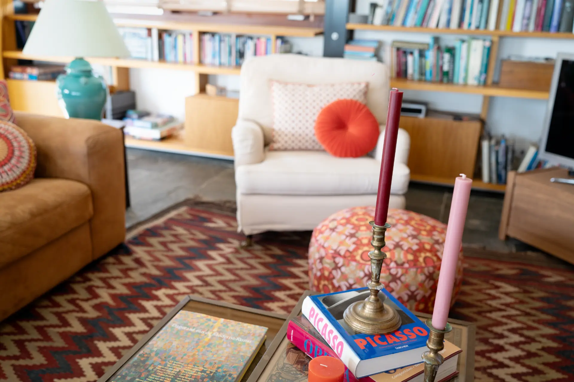 The sitting room with a white armchair, tan sofa and a red and tan zigzag rug
