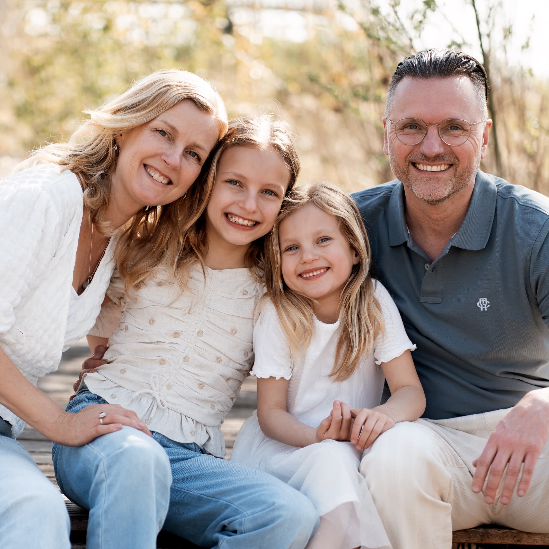 Family of four sitting close together and smiling on a wooden jetty
