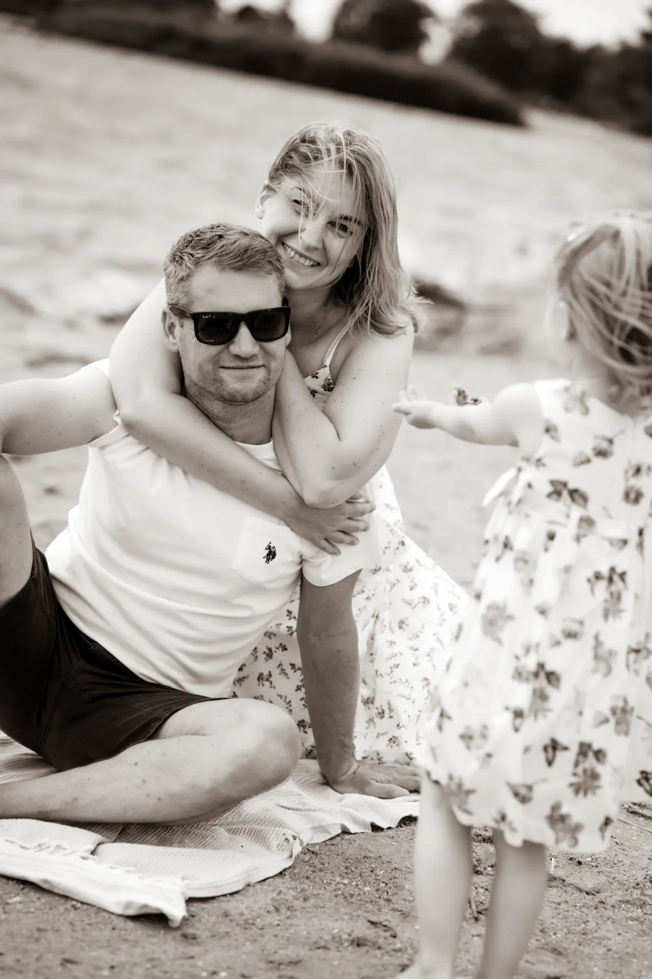 Mother hugging the father from behind on the sand as their daughter plays