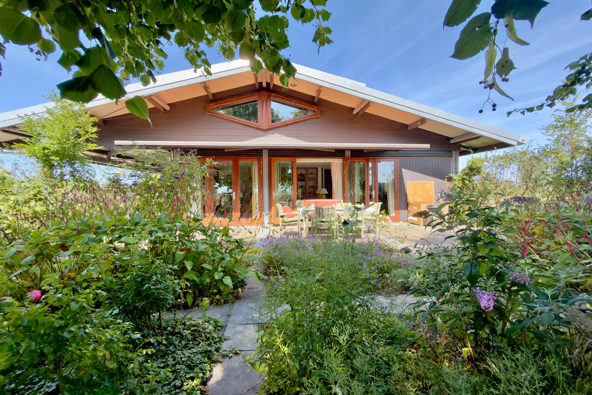 A low brown house with wide glass doors opening onto a stone patio and garden