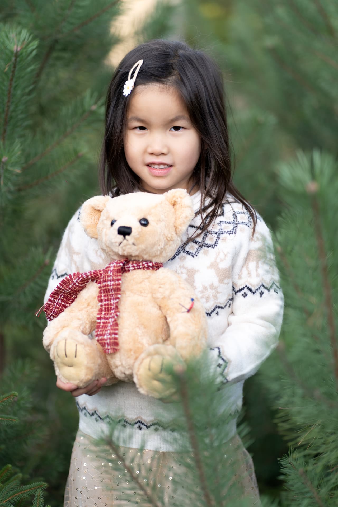 Girl holding a Christmas teddy bear among the pines