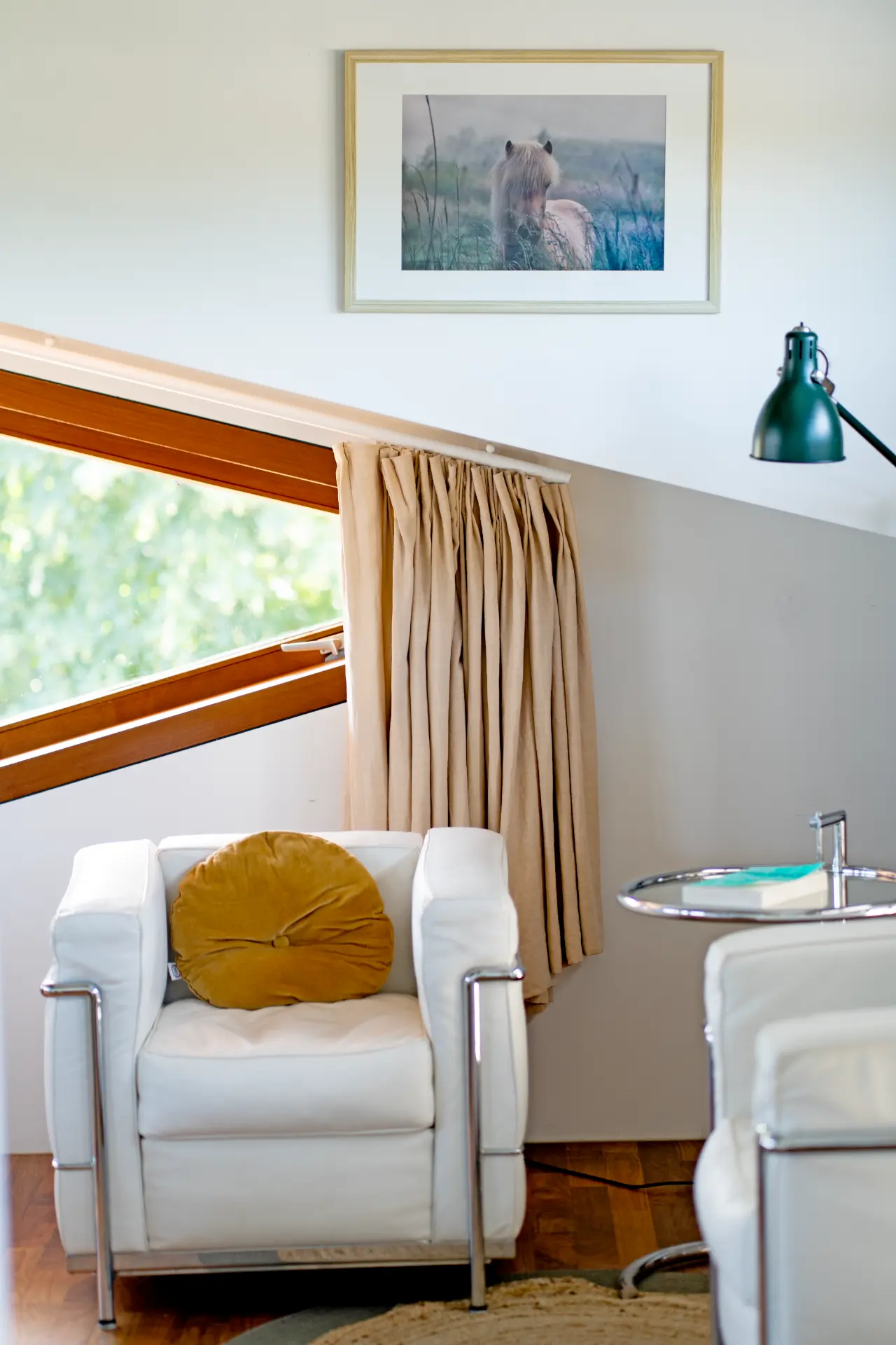 A white armchair with an ochre cushion beneath a print of a horse in the mist