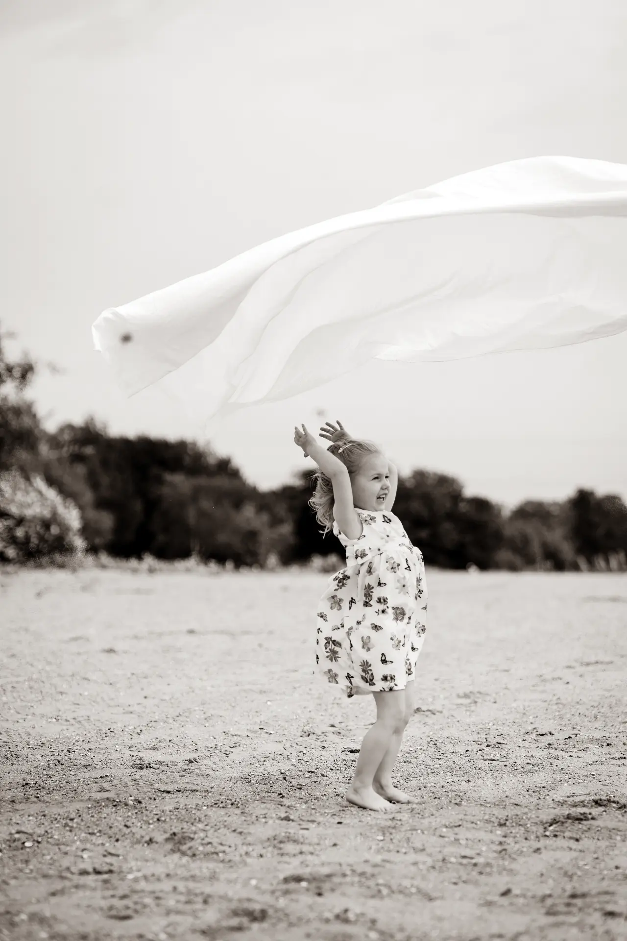 Girl with arms raised as a white sheet flies overhead