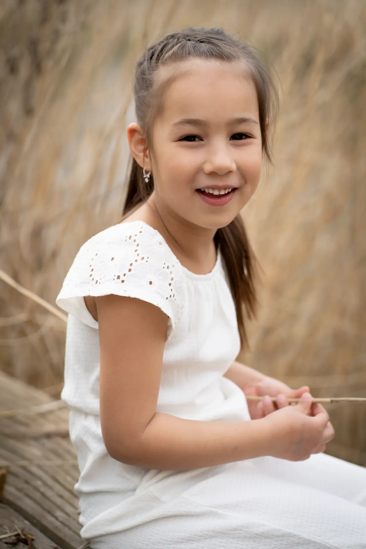 Girl in white sitting in the reeds holding a thin stick