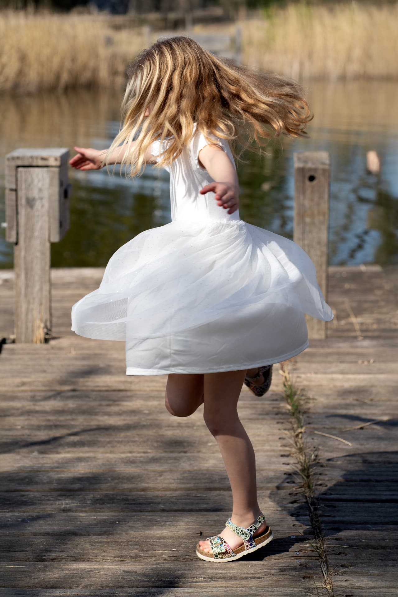 Girl in a white tulle dress spinning on the wooden jetty