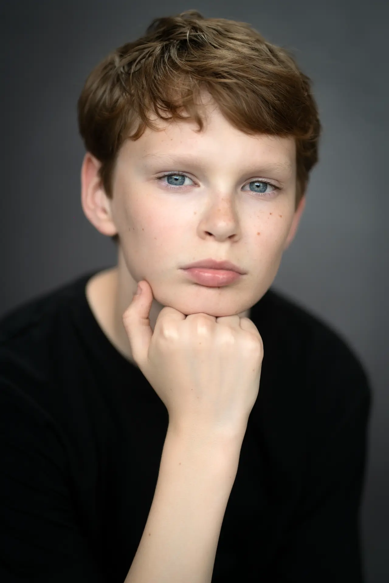 Boy in black looking into the camera against a grey backdrop