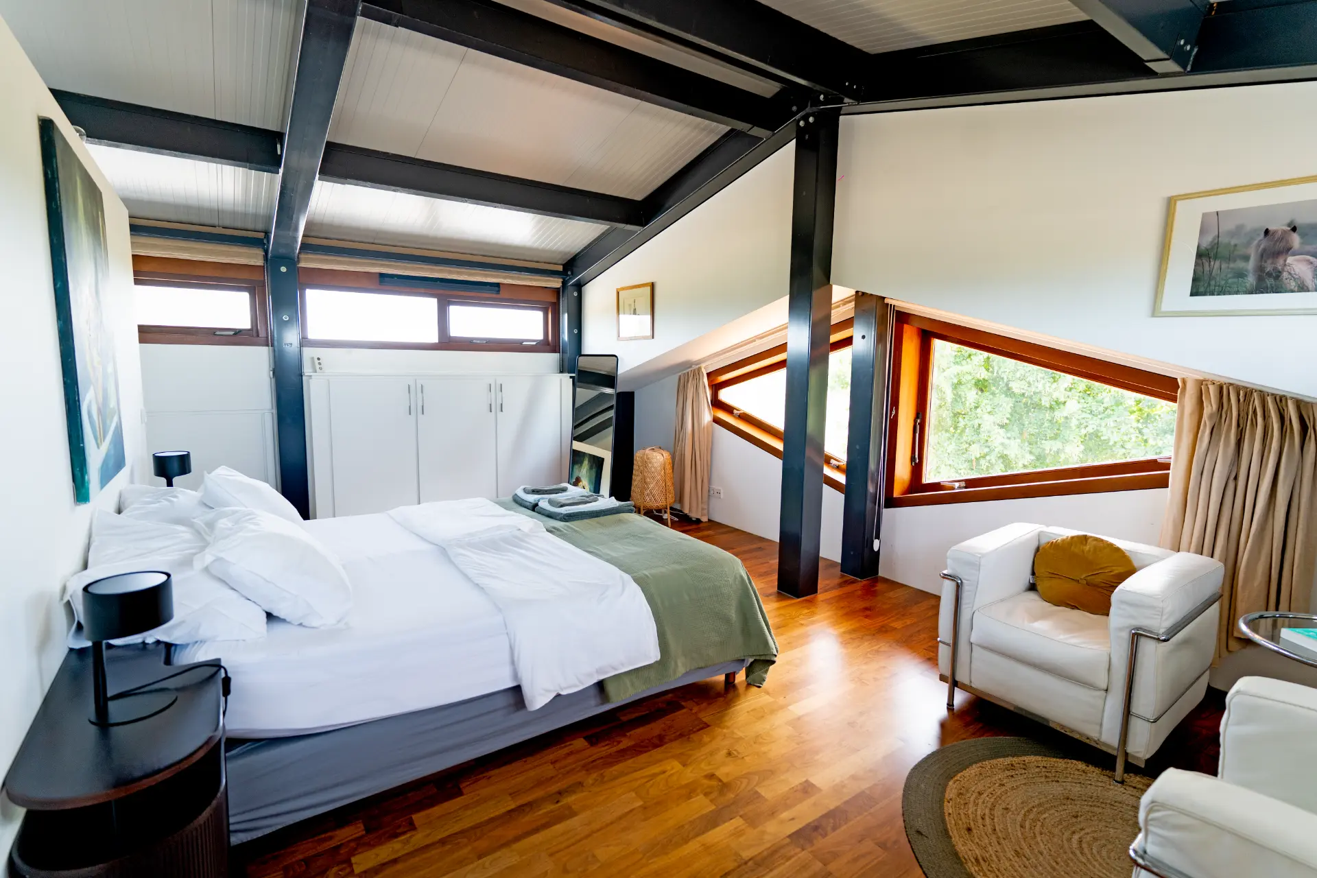 The bedroom with white linen, dark steel beams and slanted windows to the trees