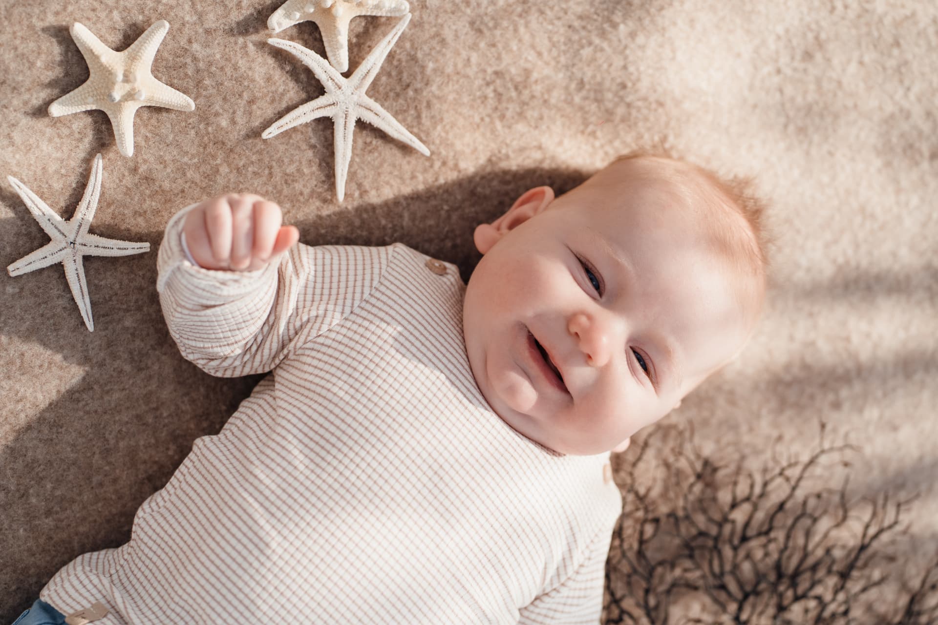 Baby lying on a sand-coloured blanket beside white starfish