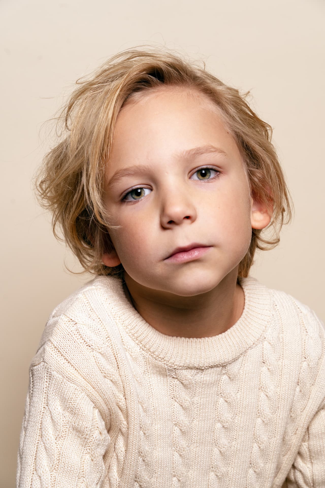 Close portrait of a blond boy in an ivory knit sweater against a warm pale backdrop