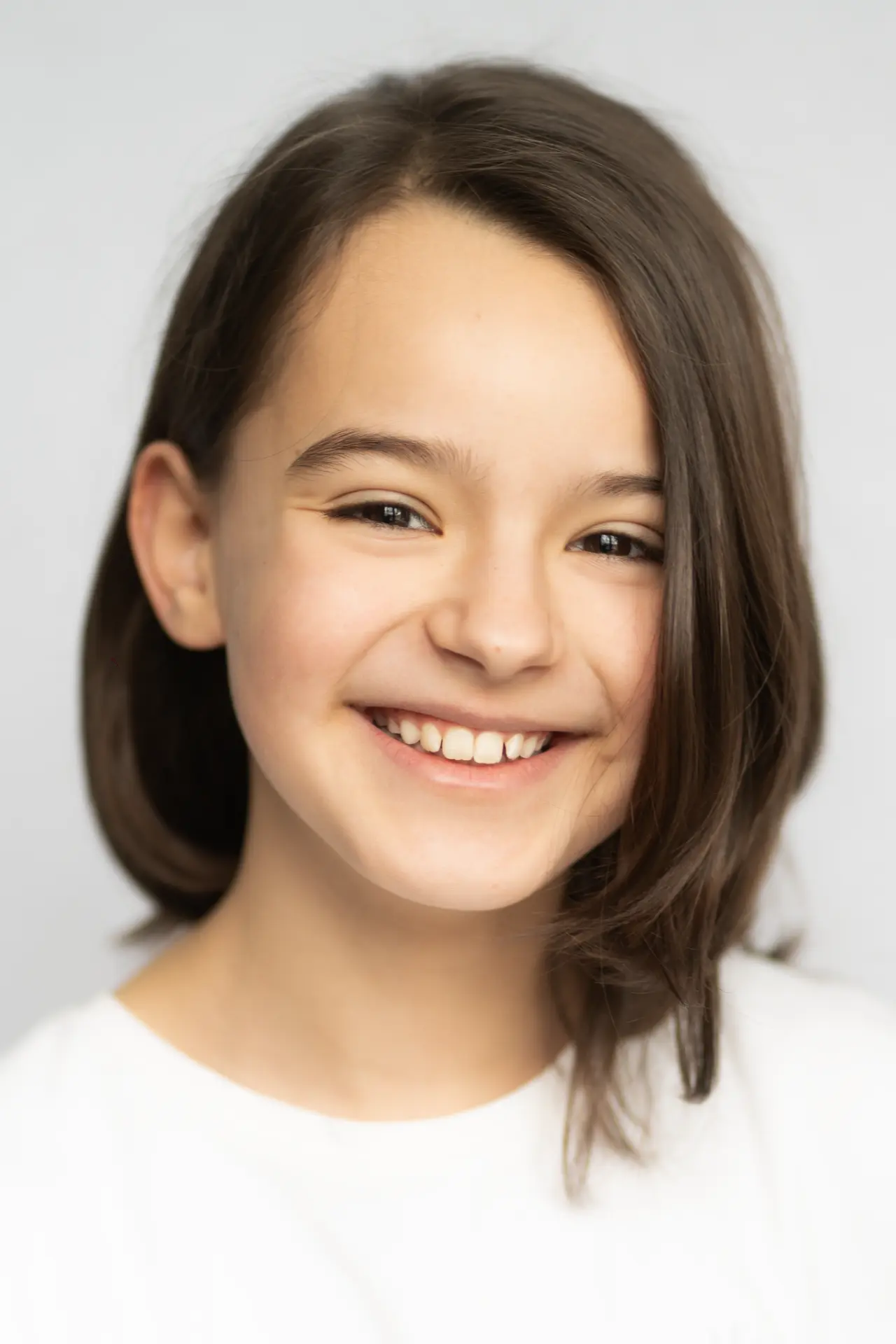 Girl in a white shirt smiling against a light studio wall