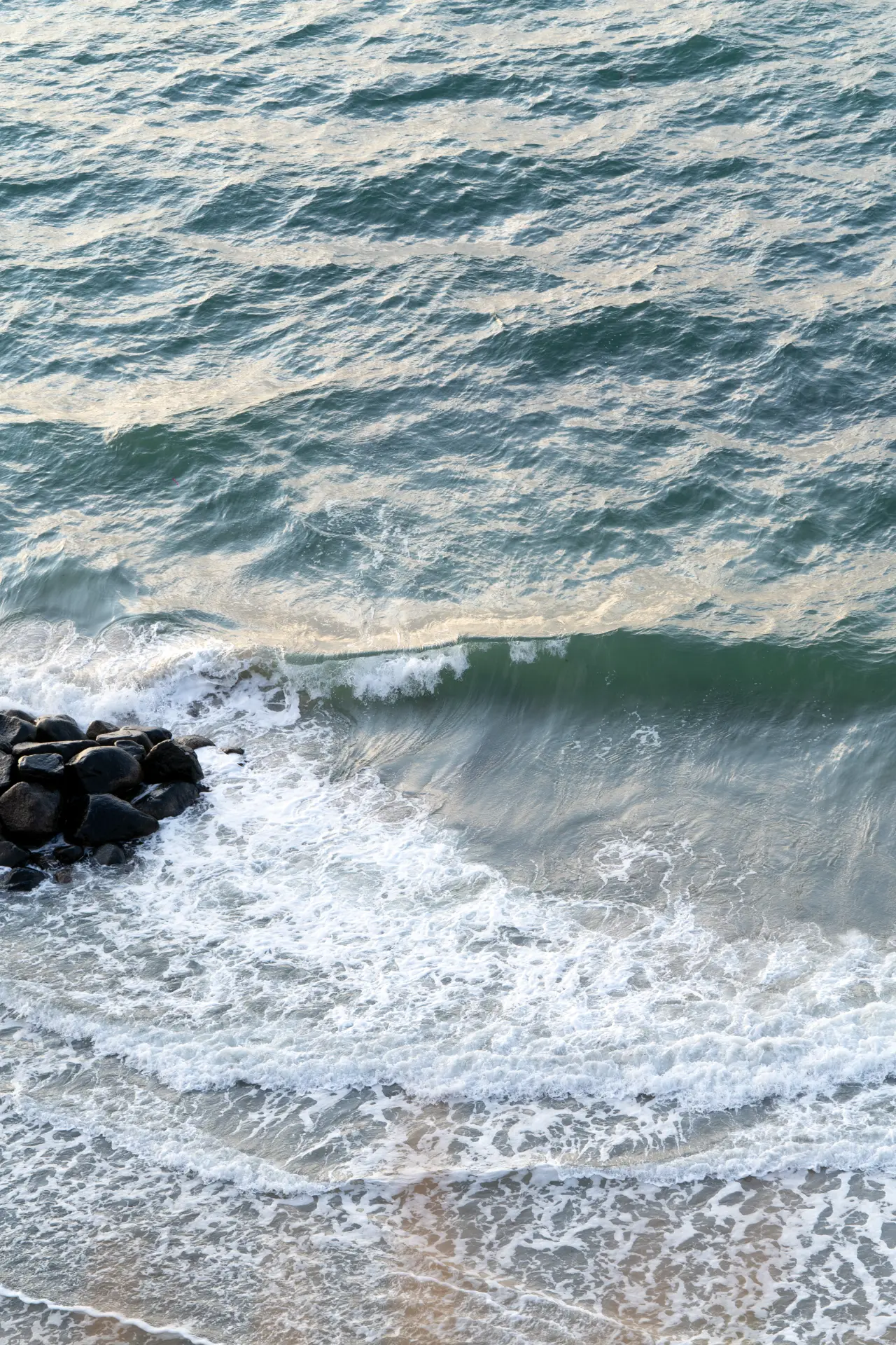 Aerial view of a wave curling onto a rocky shore