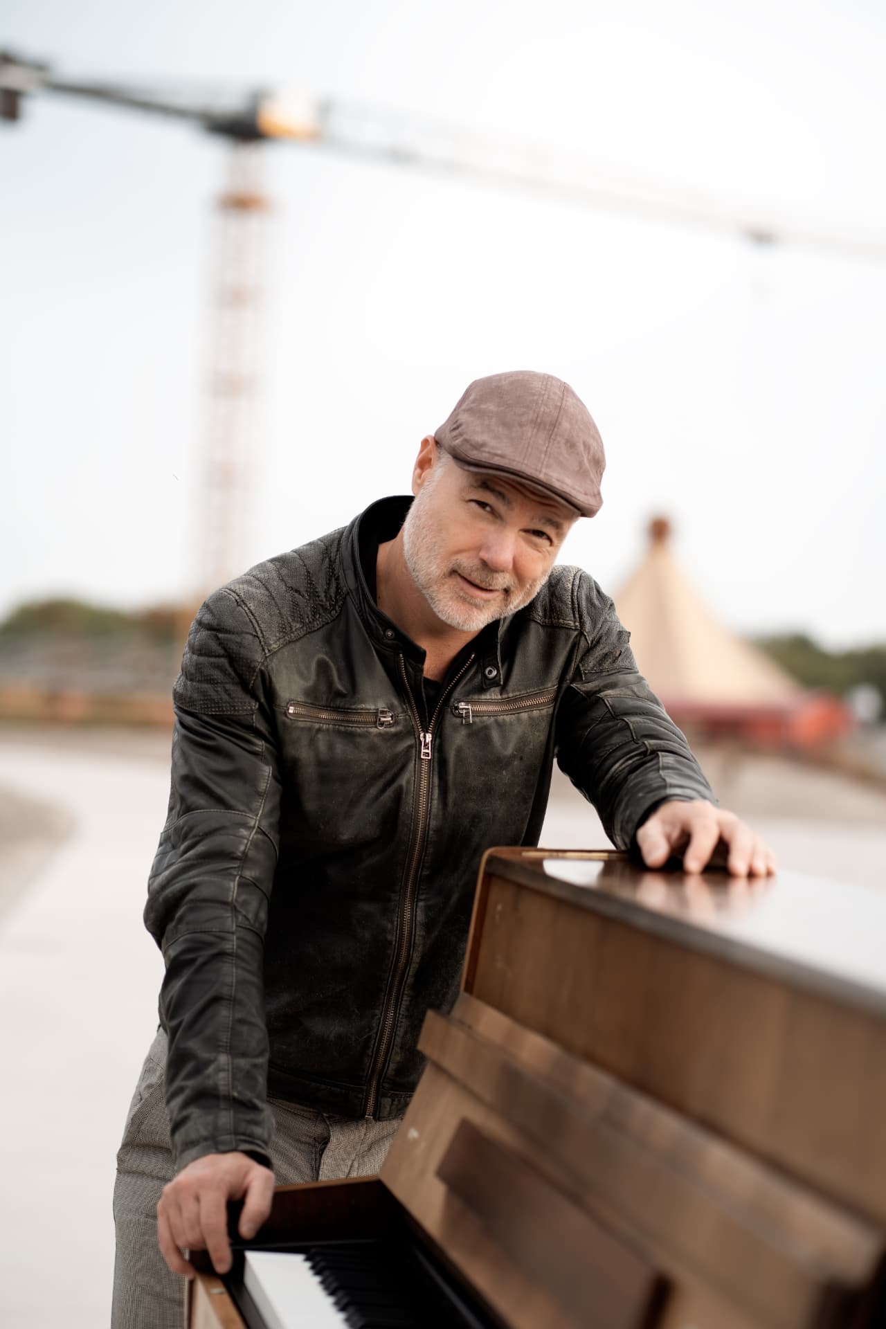 Peter smiling, leaning on his piano in bright daylight