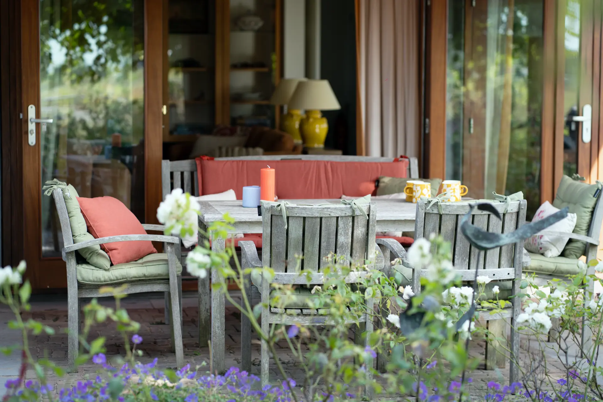 Weathered wooden table and chairs on the brick terrace, mugs and candles set out