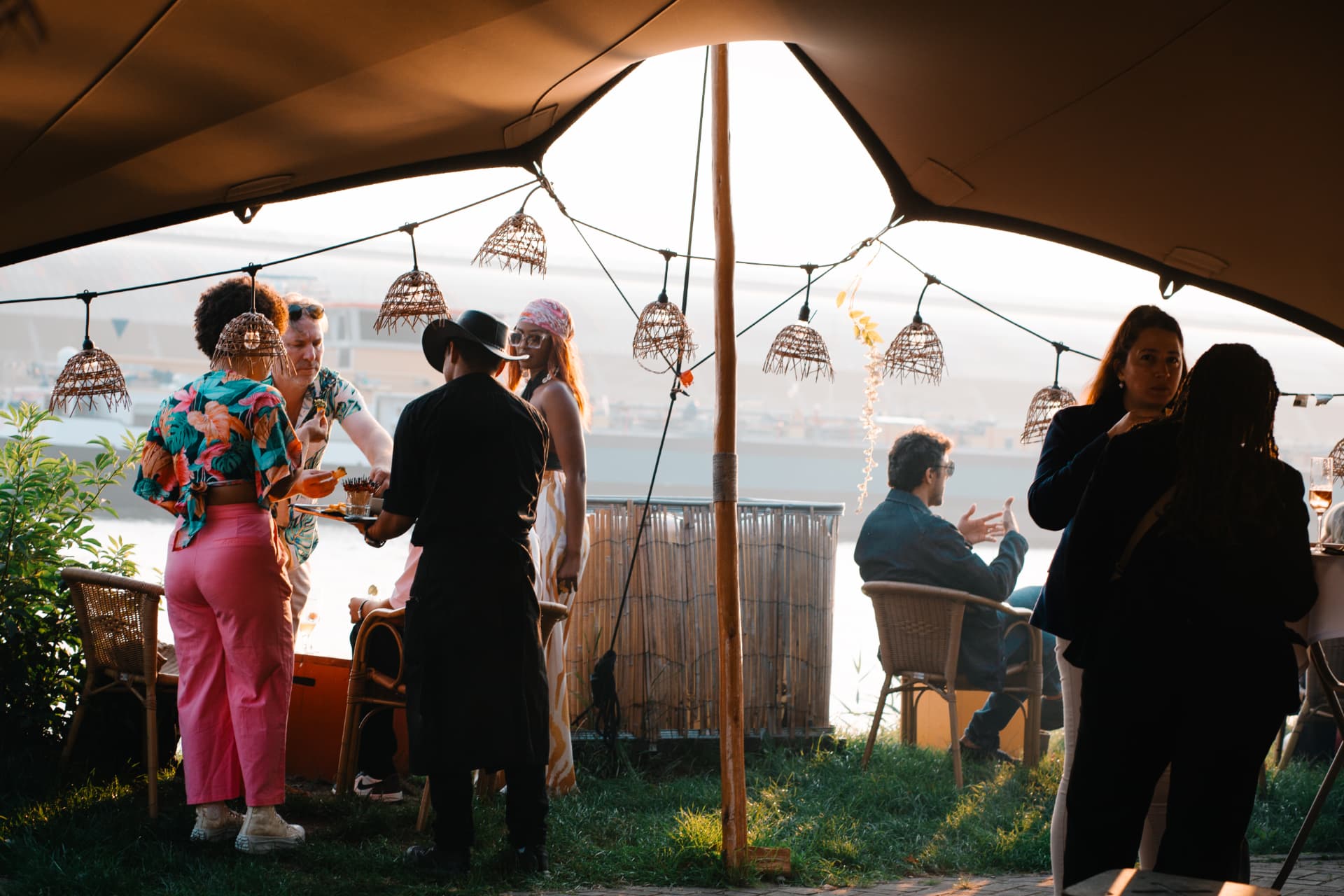 Guests gathering beneath a canvas canopy beside the water