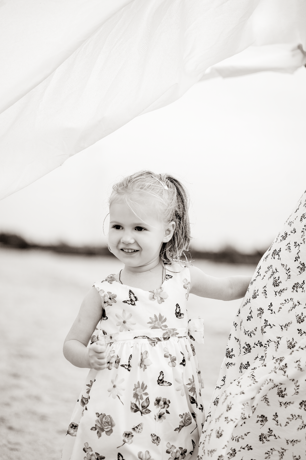 Young girl in a floral dress beside flowing white fabric on the beach