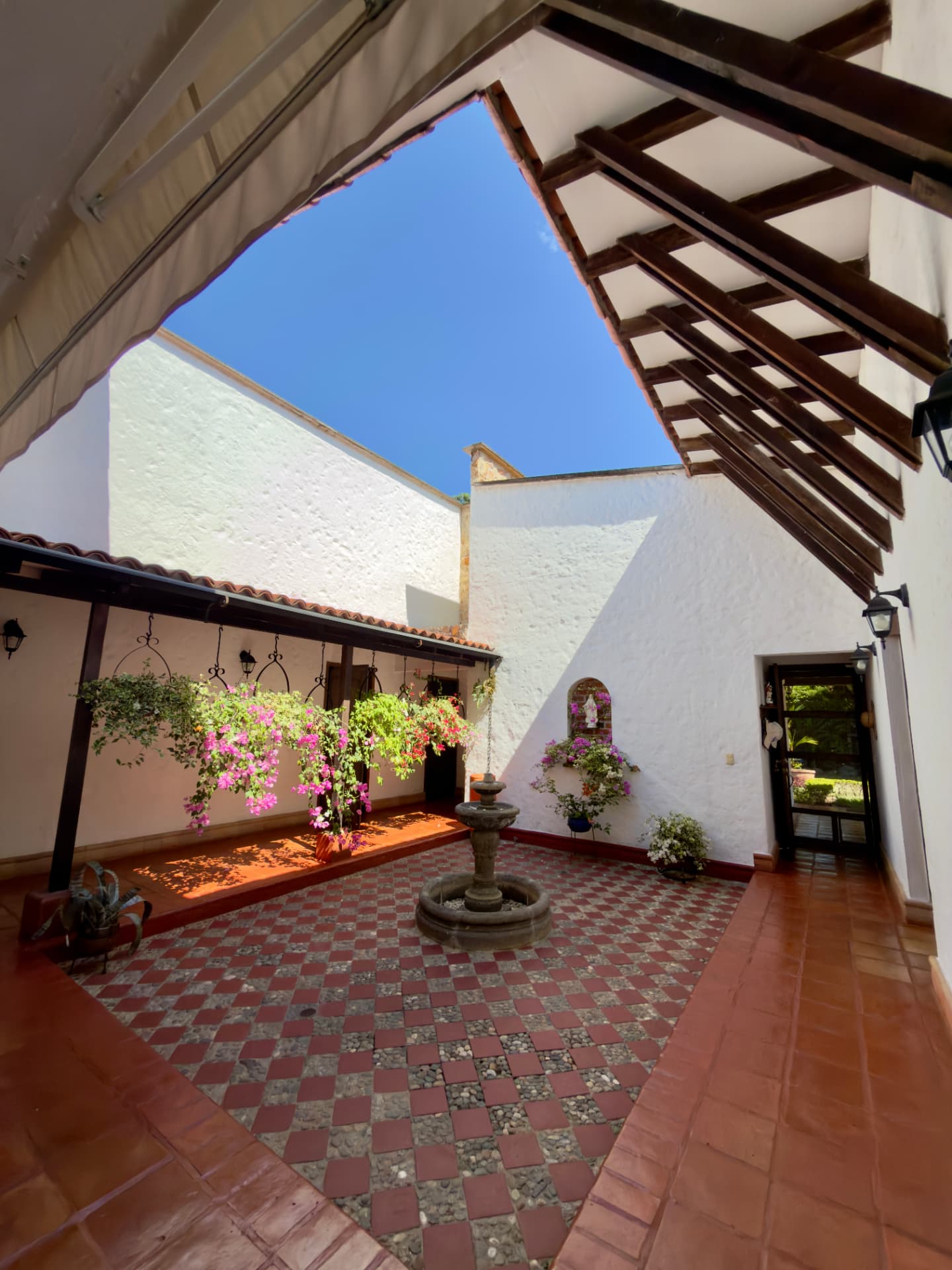 Open-air courtyard with a stone fountain, checkered tiles and hanging flowers