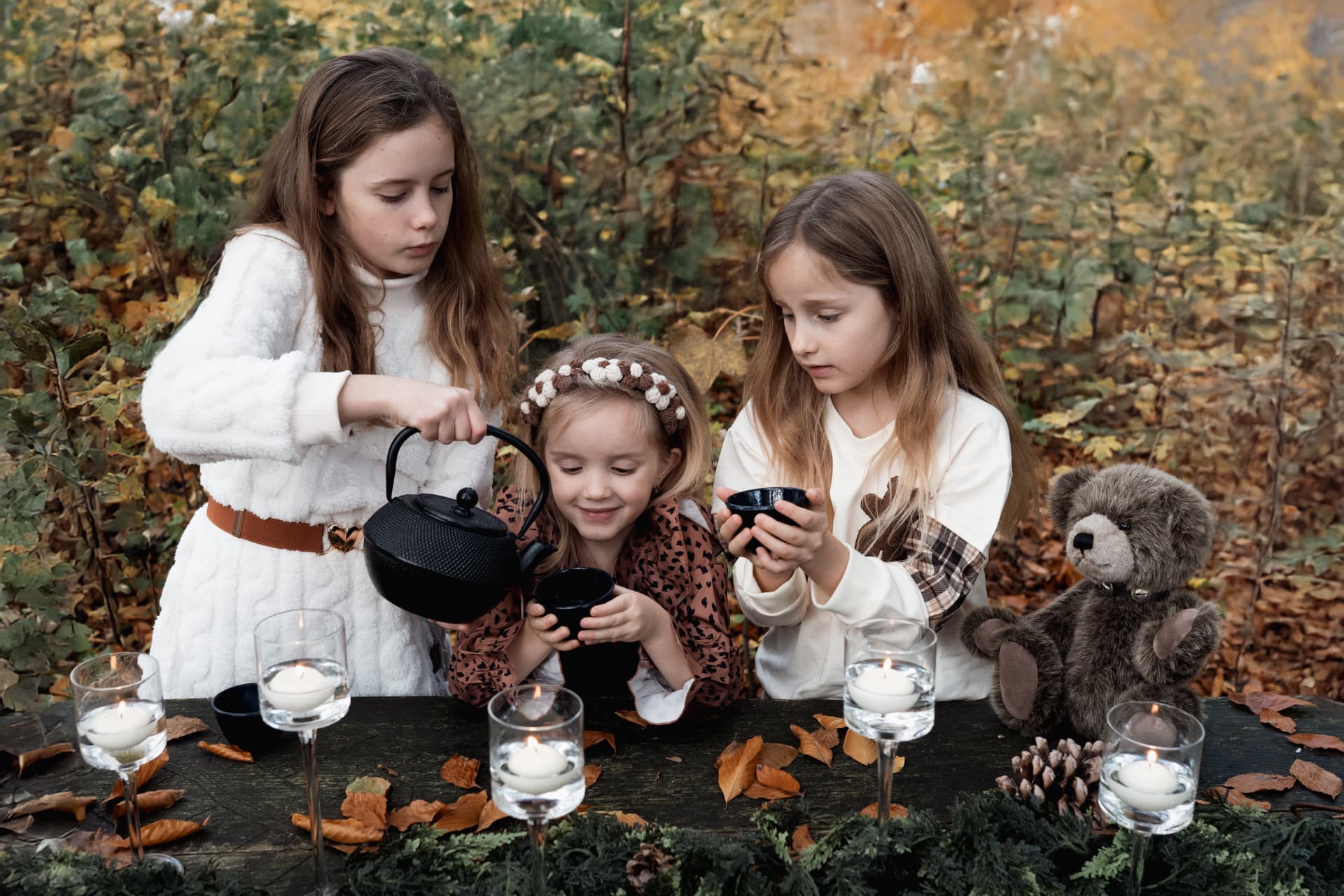 Children pouring tea beside their teddy bear