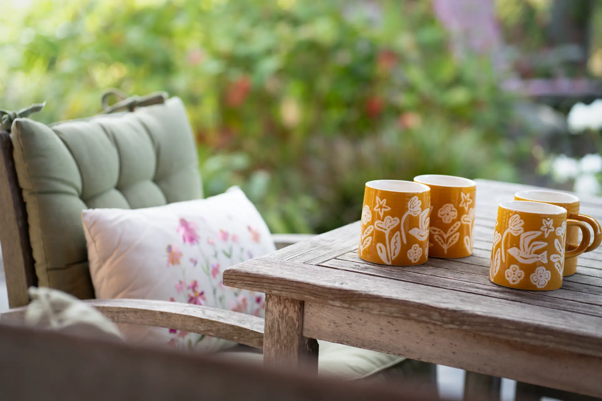 Yellow floral mugs on the wooden table with the garden soft behind