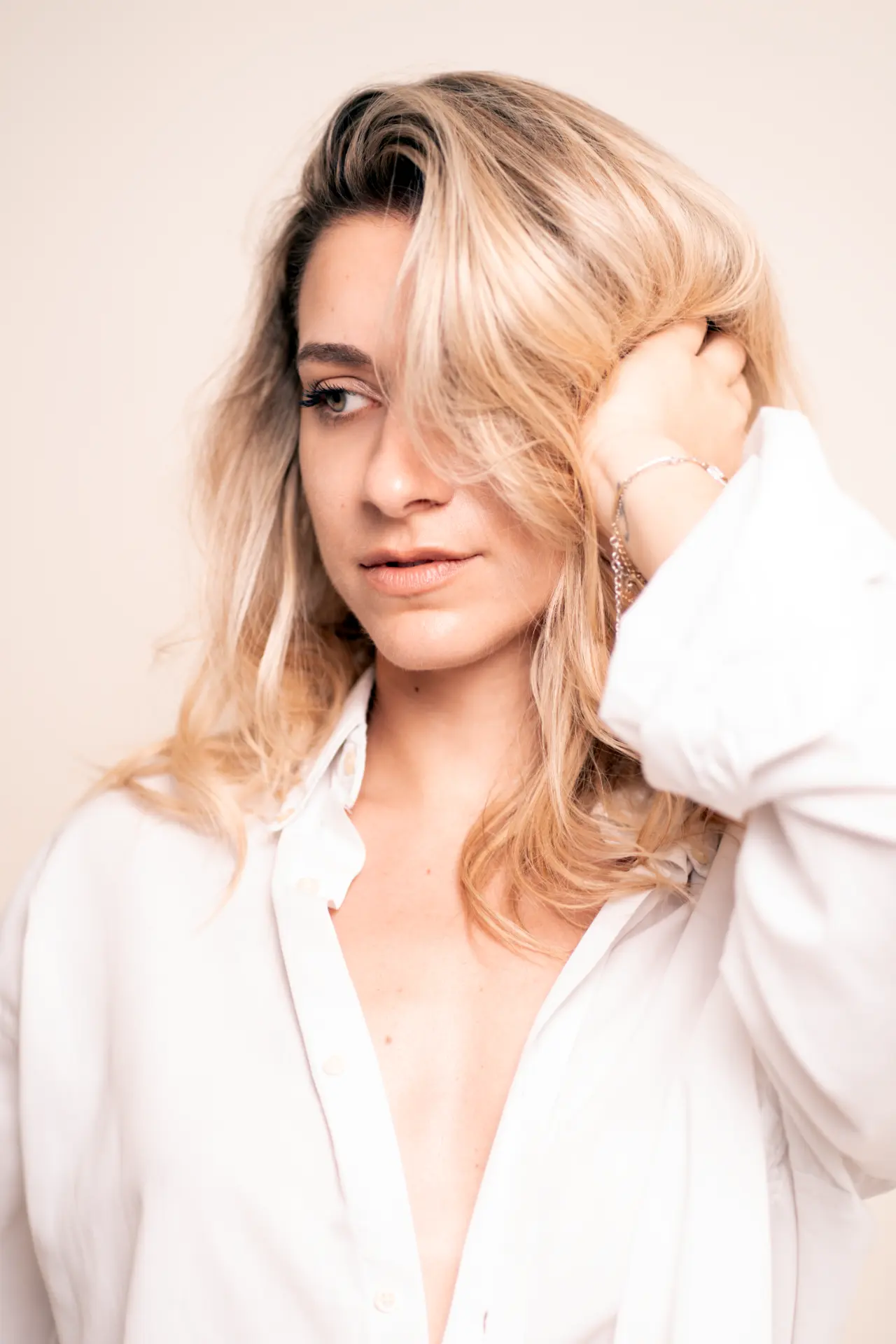Lia in a white shirt looking into the camera, hand lifted to her face