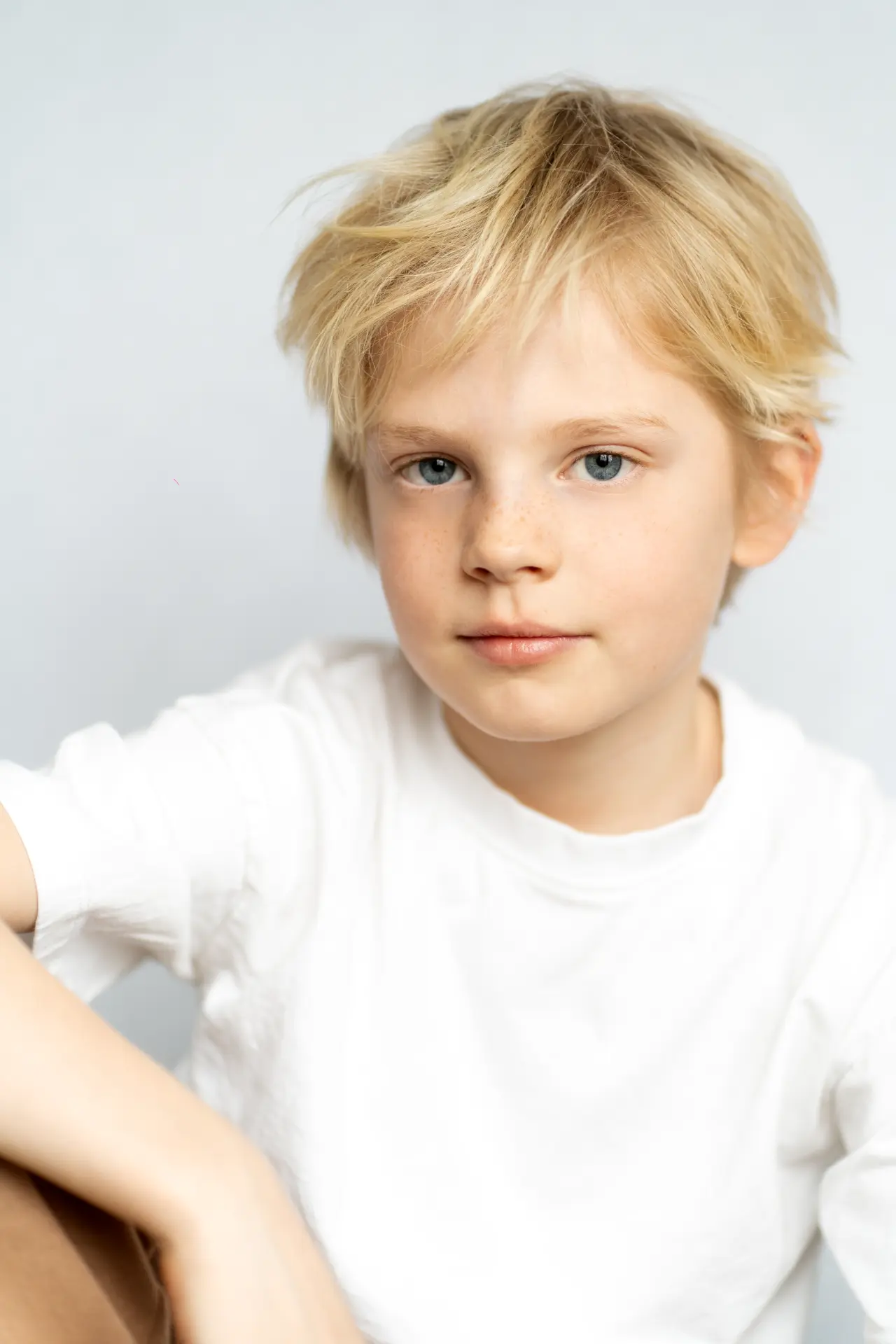 Blond boy in a white shirt against a soft white studio wall