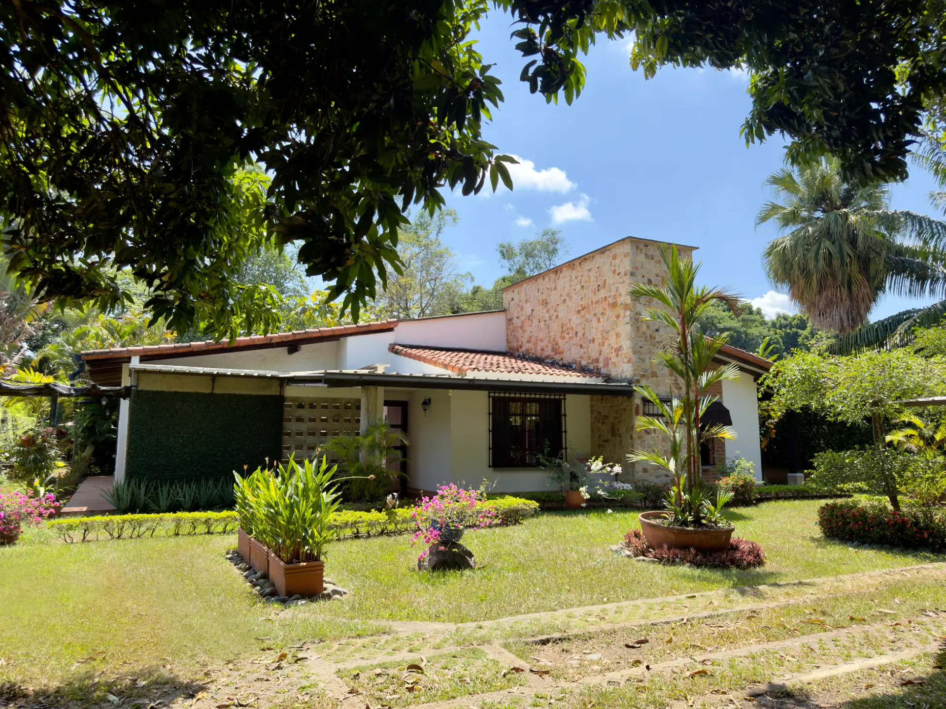 White facade with a stone tower and terracotta roof seen across the lawn