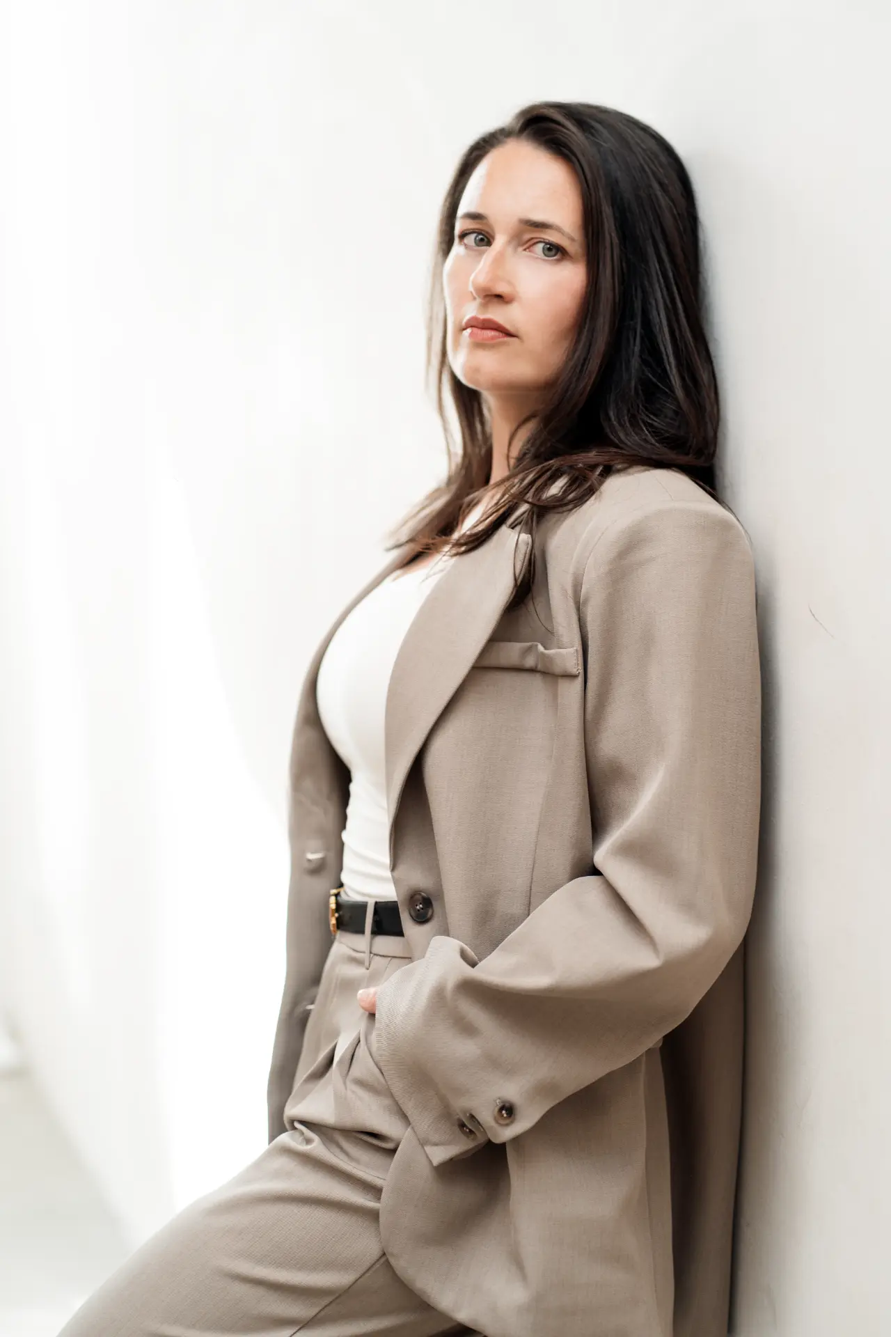 Suzana leaning against a wall in a tailored suit